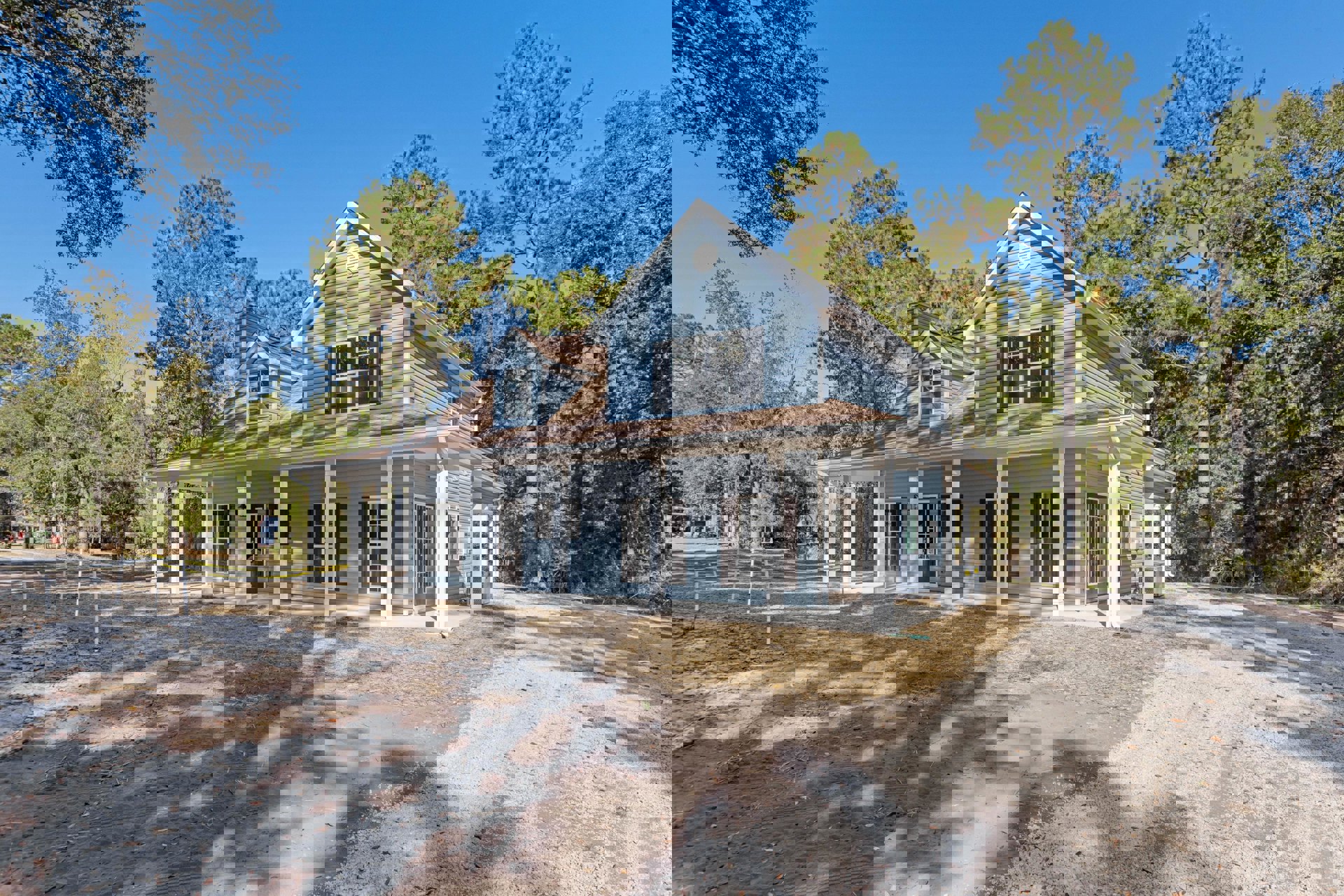 Two-story custom home with white-framed windows, covered front porch, landscaped yard, and mature trees surrounding the property.