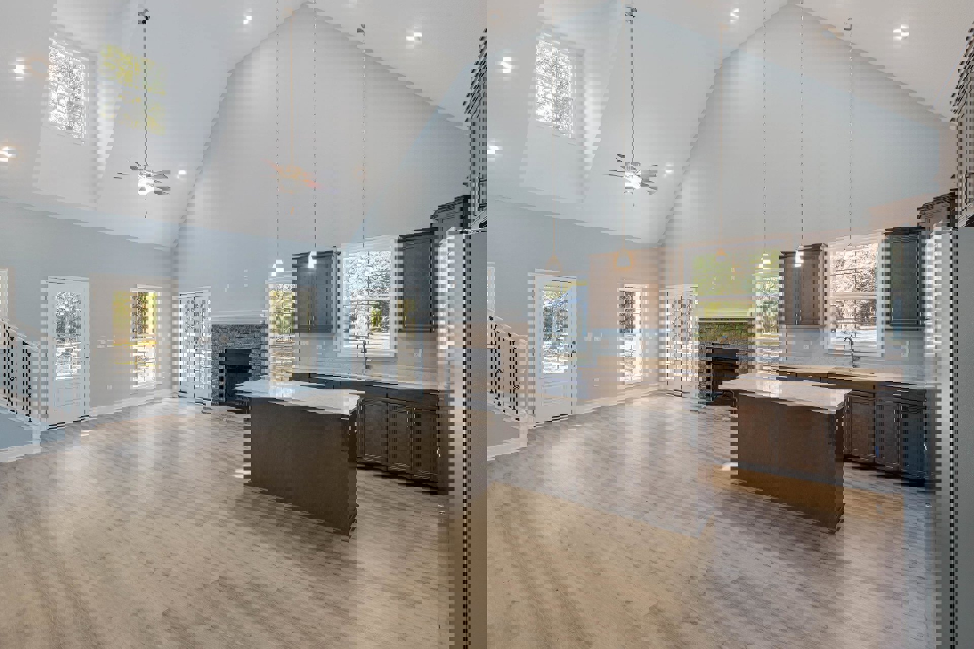 Open-concept kitchen with a central island featuring stone countertop, white cabinetry, stainless steel appliances, hardwood flooring, and a fireplace with a white mantel; double