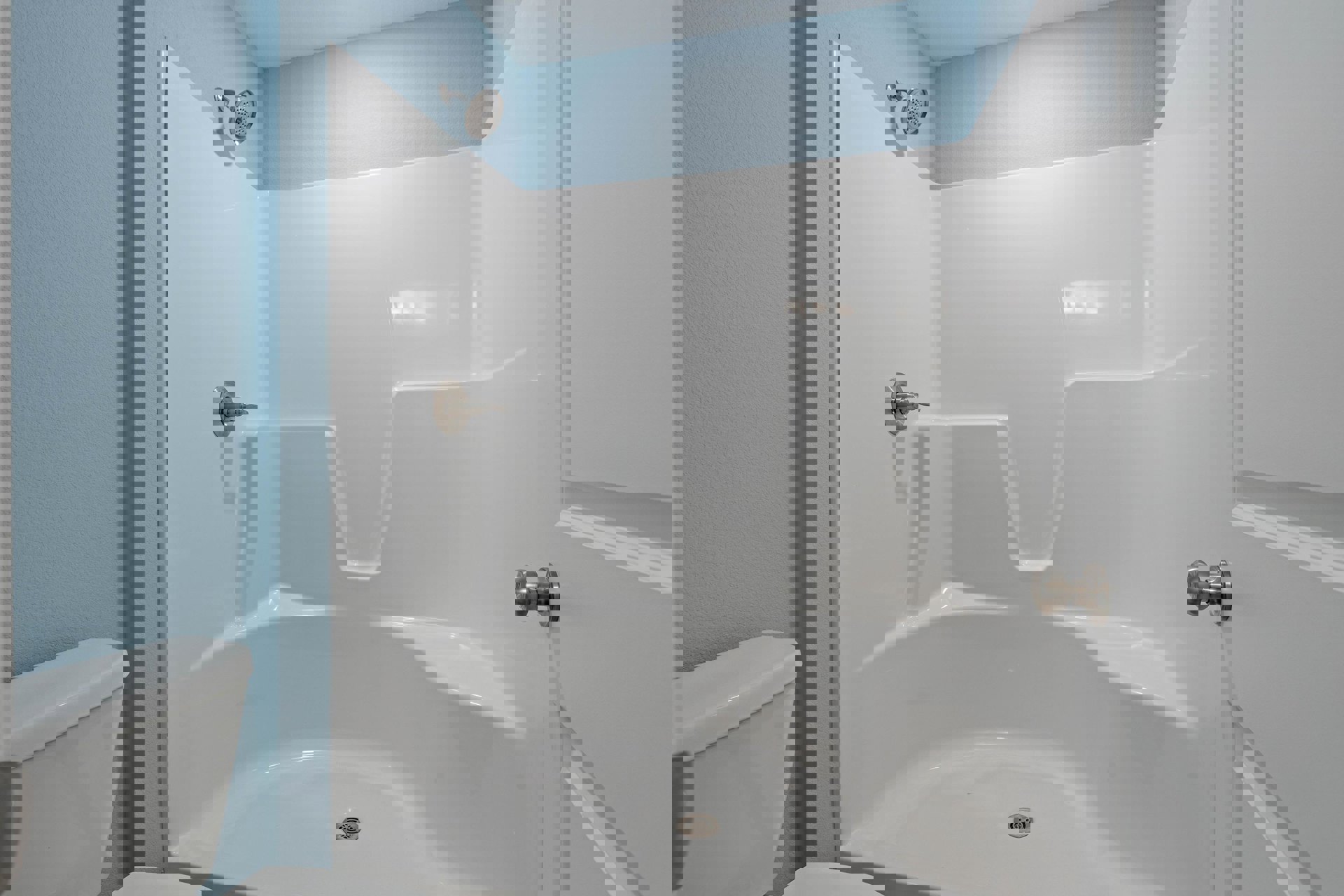 White tile shower with silver fixtures and showerhead, adjacent to blue accent wall and white toilet tank.