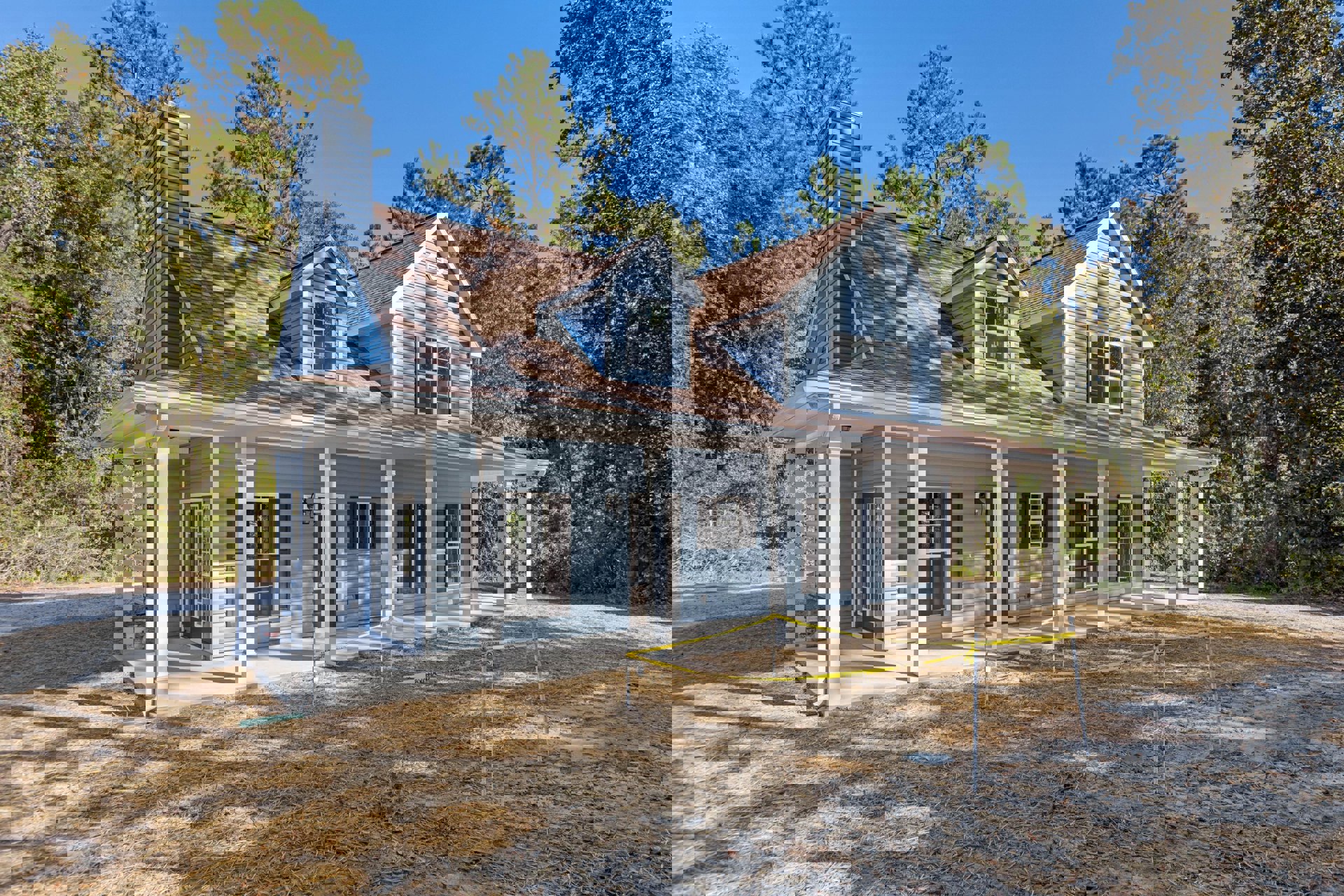 Spacious porch with white railings, prominent brick chimney, fenced yard with yellow caution tape, large windows reflecting surrounding trees, close-up views of entry door and