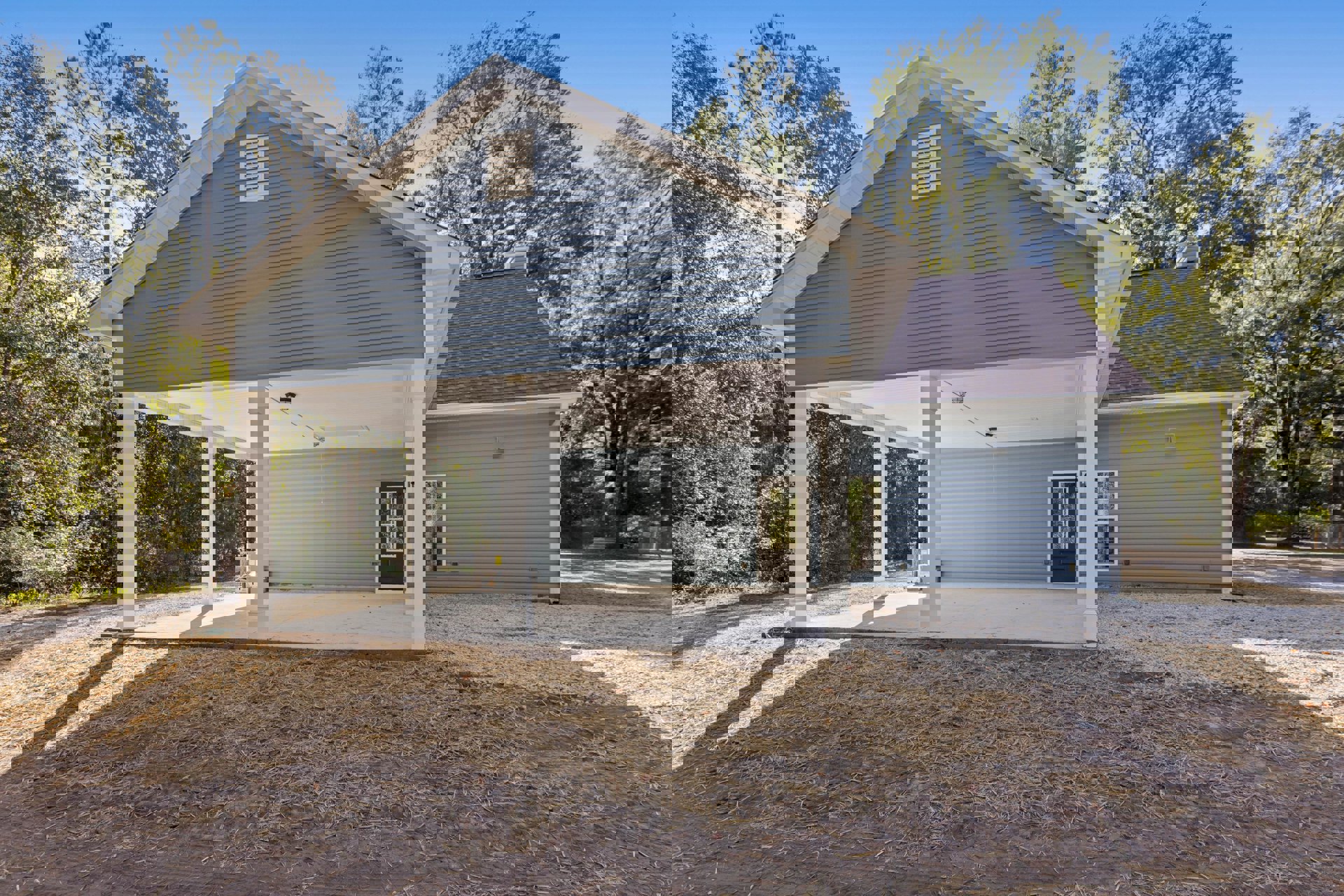 Blue-sided house with covered patio, white vent, glass-paneled door, straw-covered ground, and gray shingle roof.