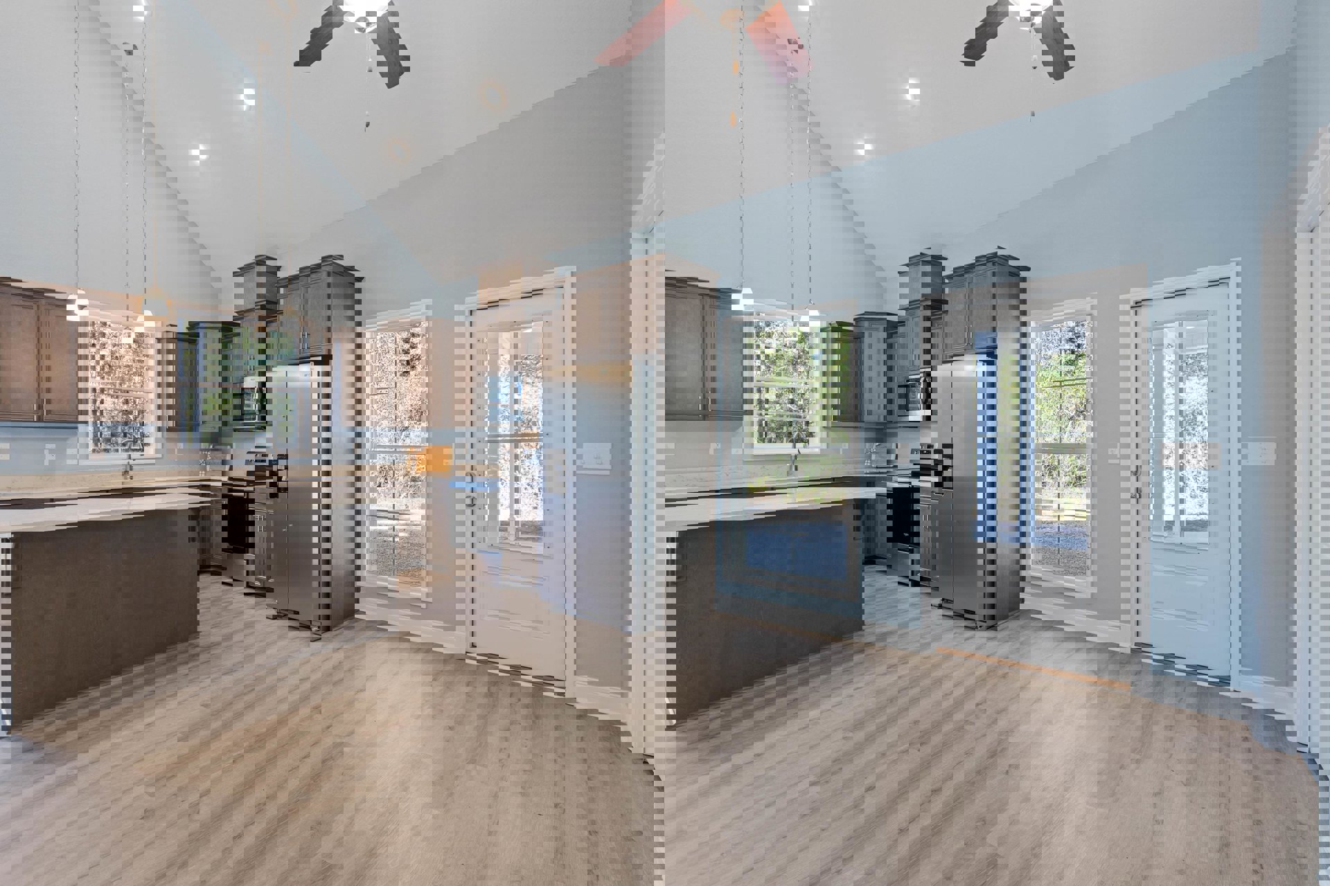 Open kitchen and dining area featuring hardwood floors, ceiling fan, stainless refrigerator with coffee maker, white glass-paneled door, window overlooking trees, built-in