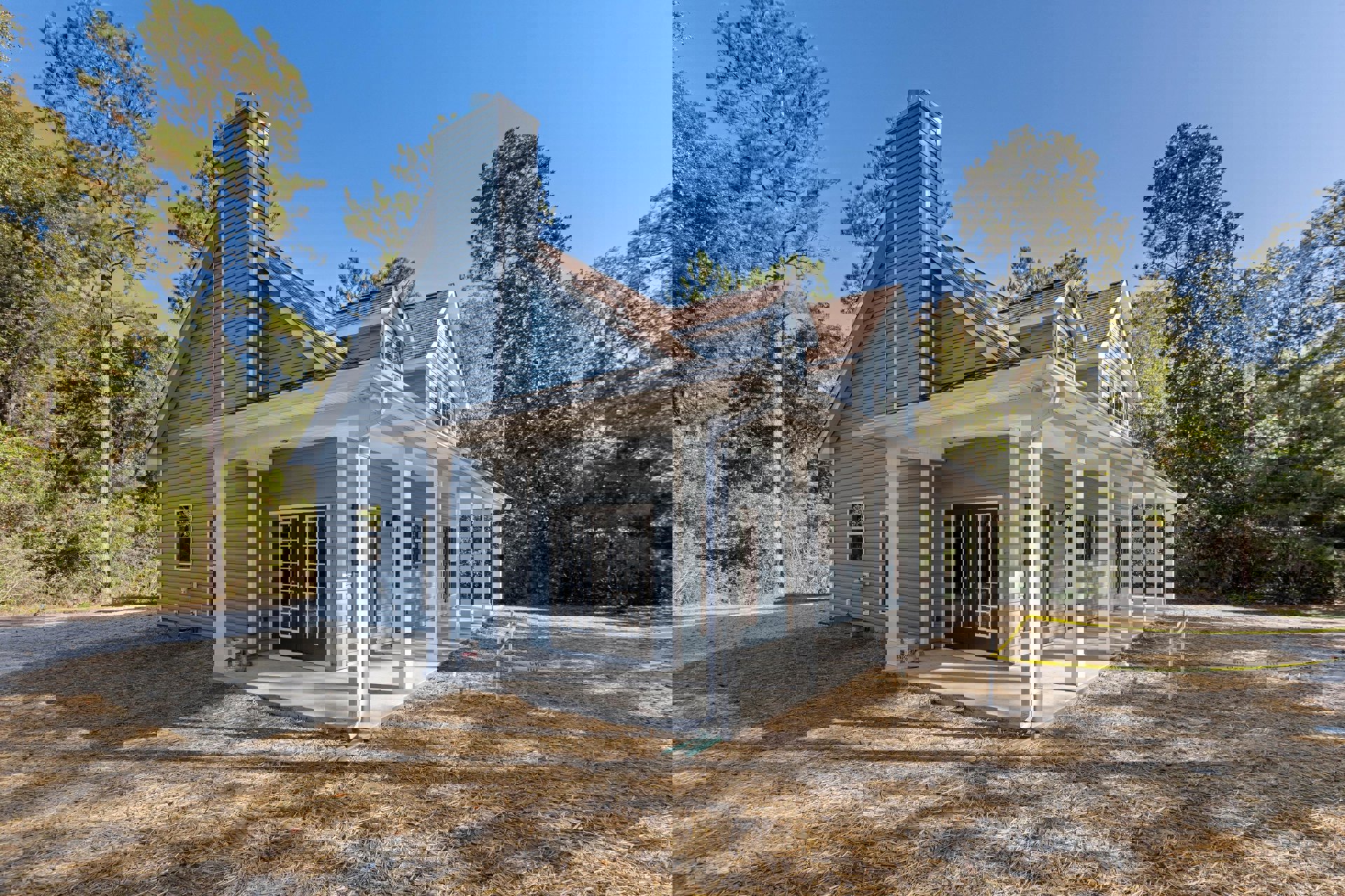 White-roofed house with double front porches, brick chimney, large windows, and tall leafy tree in landscaped yard