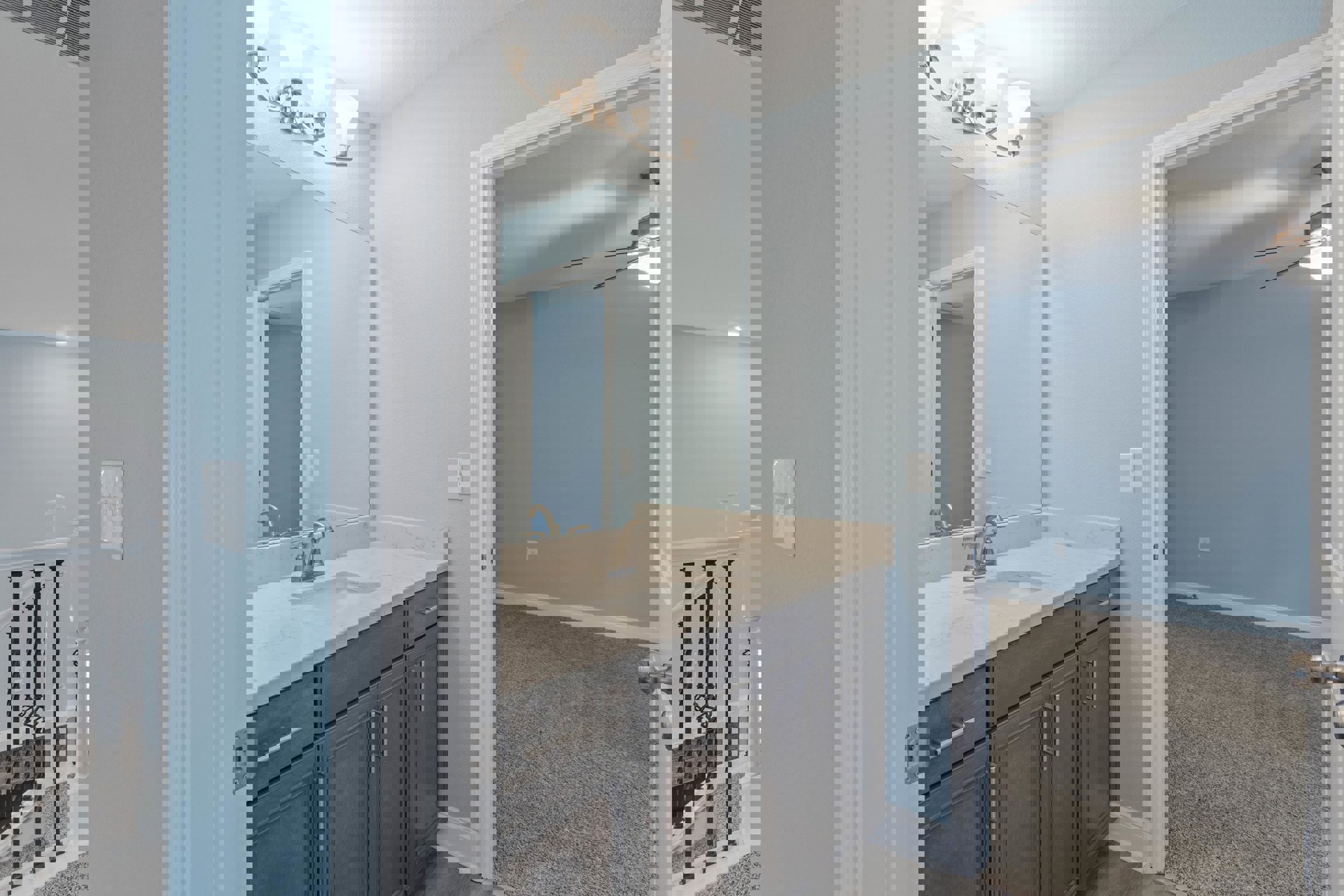 Modern bathroom with rectangular mirror above white sink, chrome faucet, tiled backsplash, light fixture with multiple bulbs, white shelf with hooks, and metal railings.