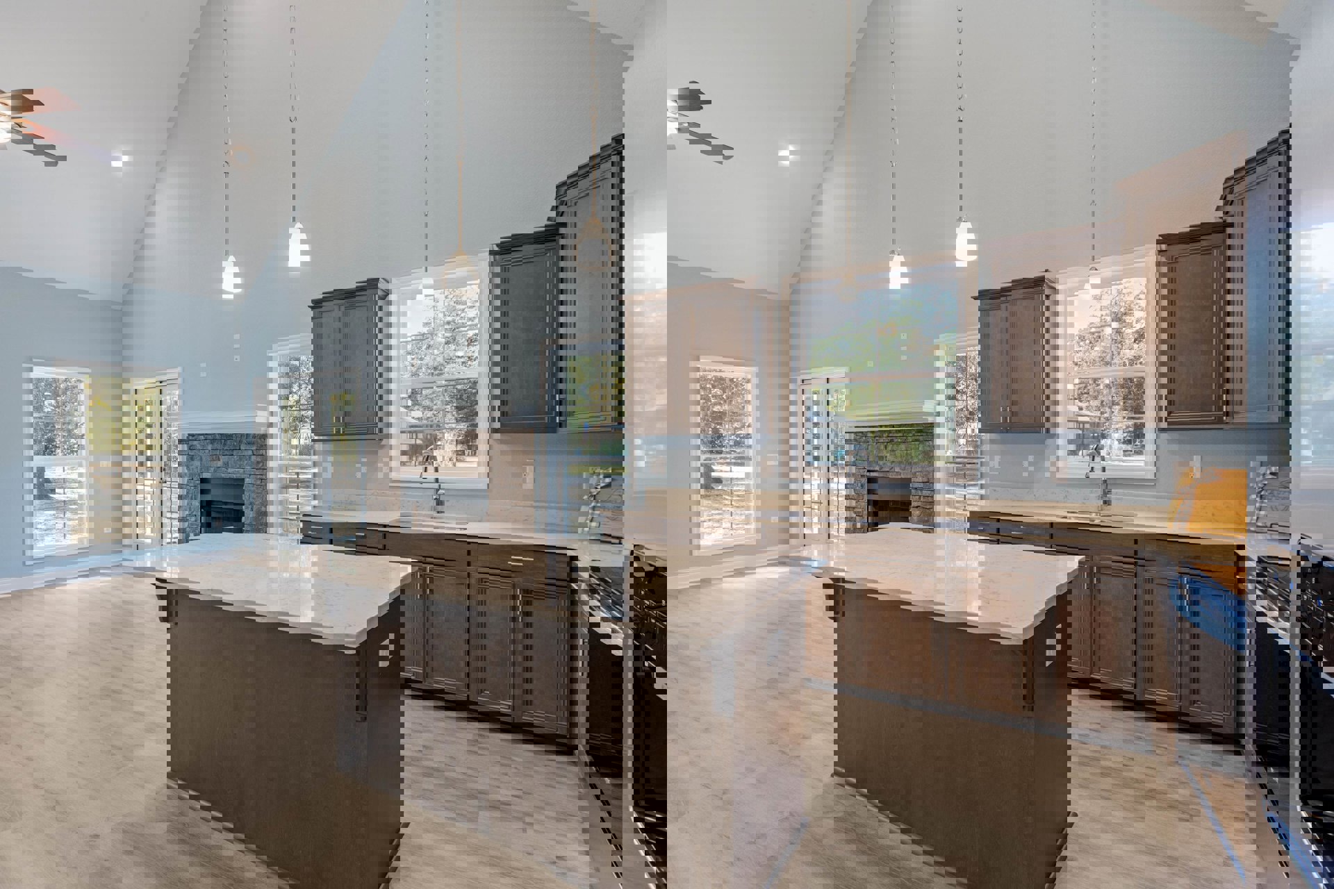 Kitchen with stone fireplace, large central island featuring wood cabinetry and stone accents, window overlooking tree, white-shaded wall light fixture, hardwood flooring, and