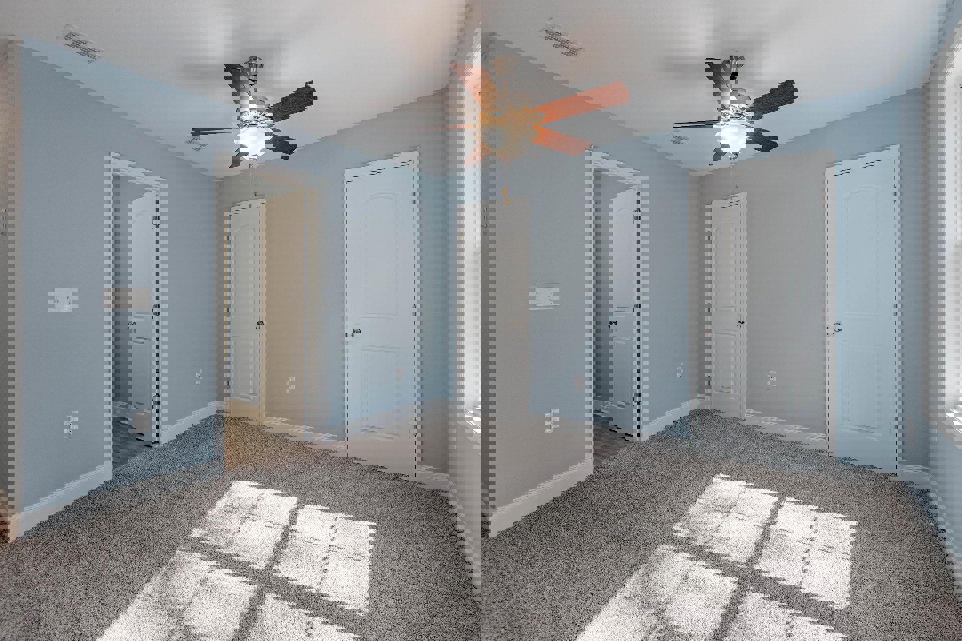 Carpeted room with two white doors, silver door knobs, ceiling fan with light fixture, window, close-up lamp, and light switch on neutral wall