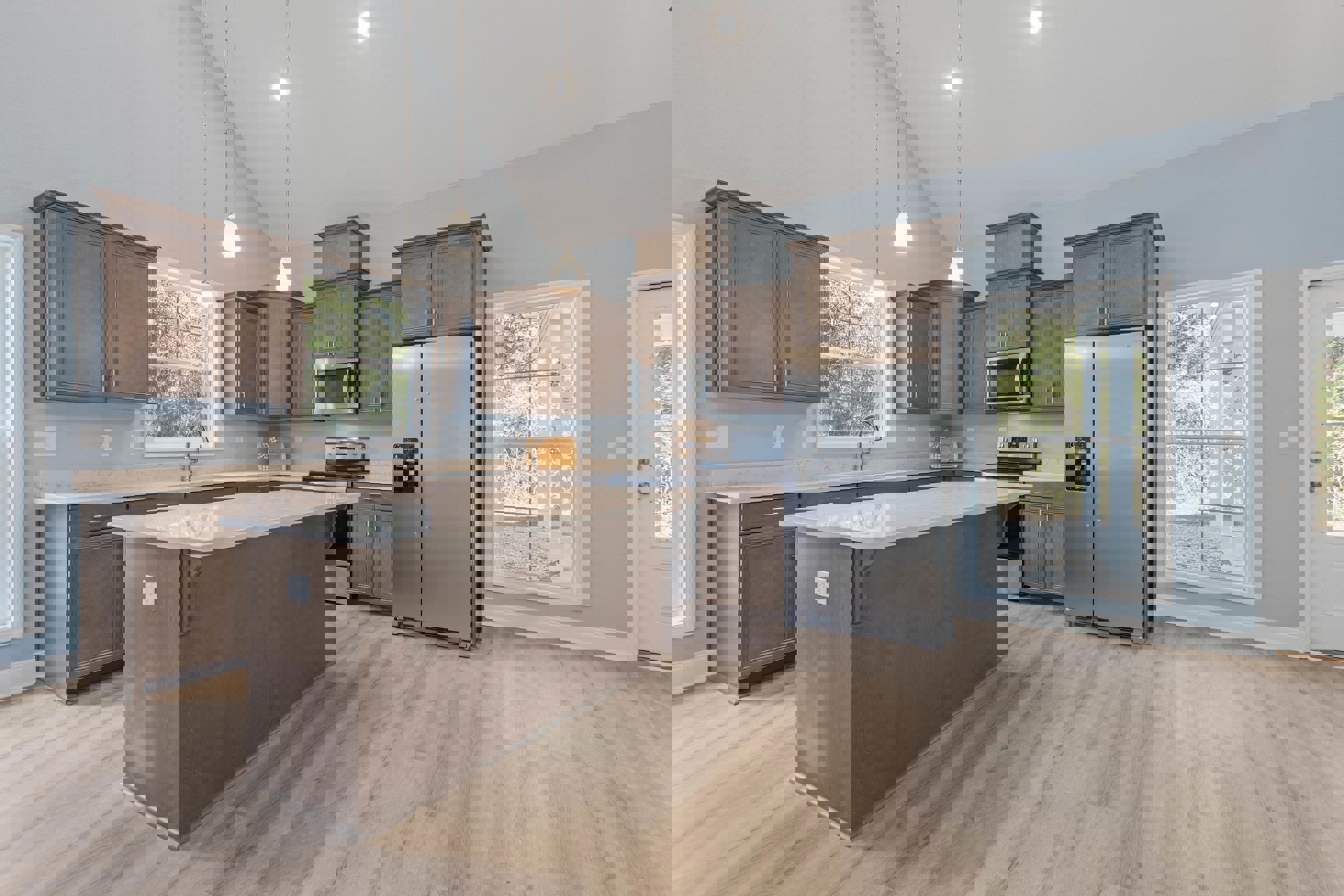 Spacious kitchen featuring a large central island with wood flooring, stainless steel refrigerator, built-in microwave, white cabinetry, stone countertops, and a window overlooking