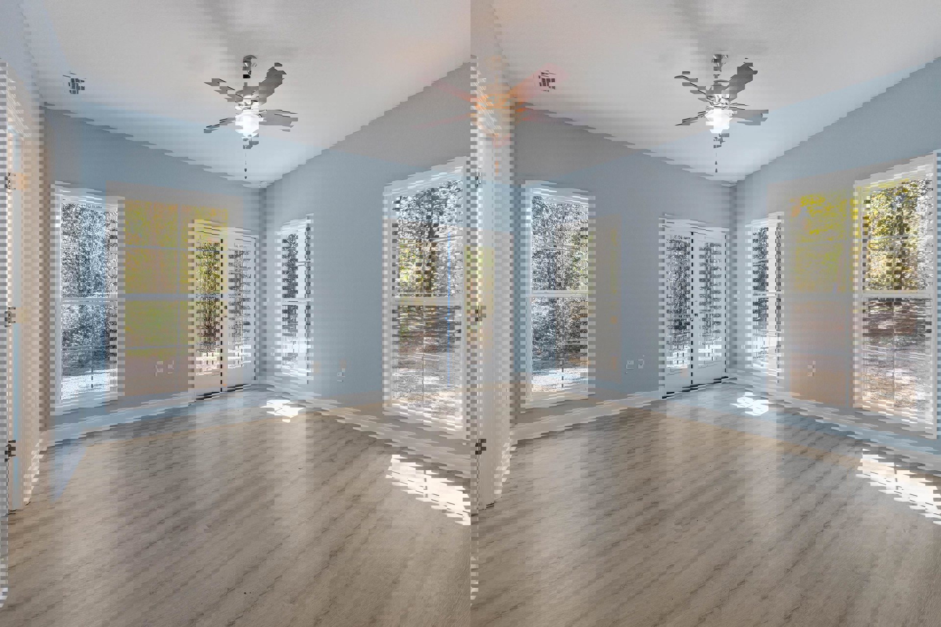 Ceiling fan with light fixture centered in a room featuring wood laminate flooring, white walls with crown molding, double glass-paneled doors, and large windows framed in white