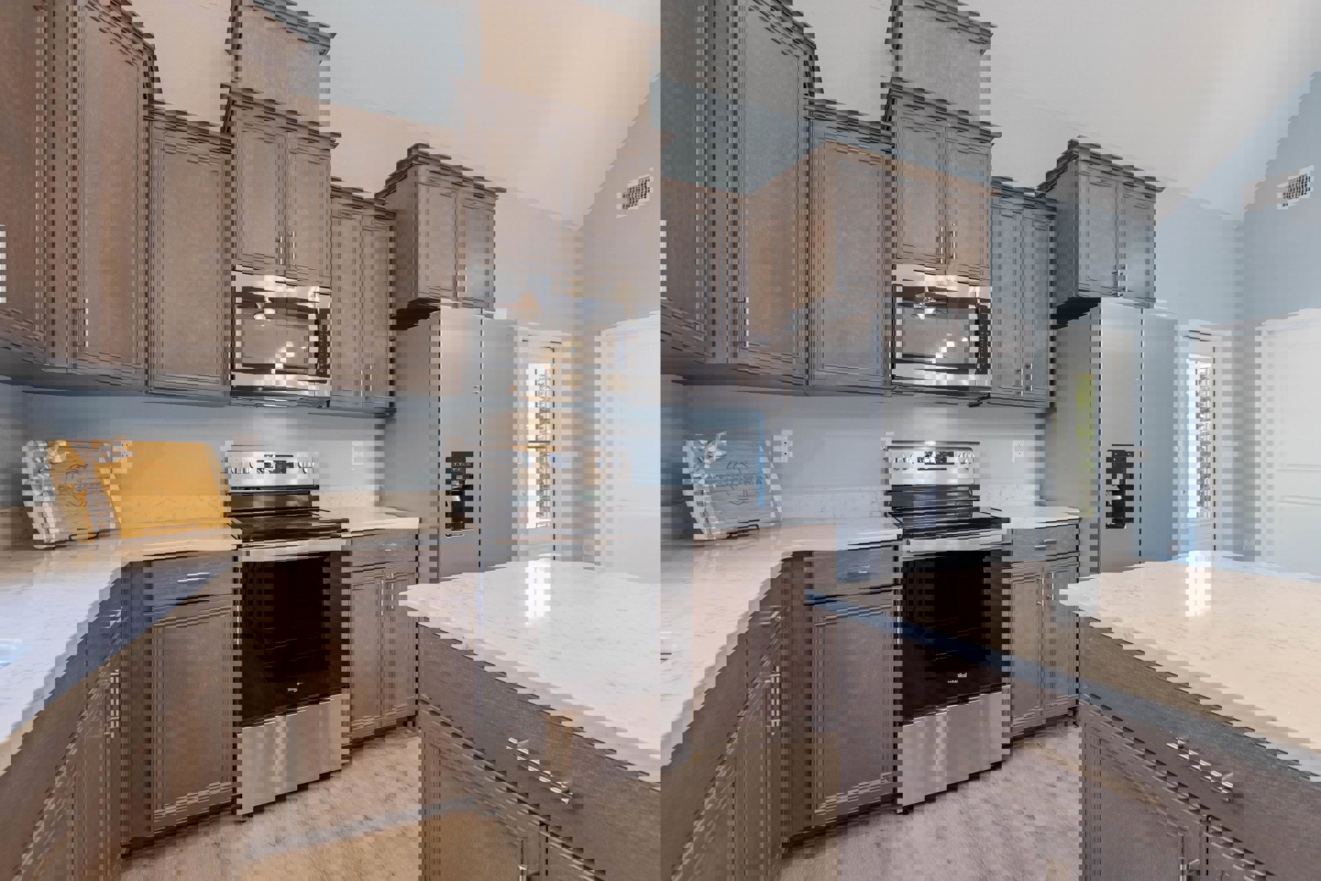 Kitchen featuring stainless steel stove and refrigerator, black and silver oven, built-in microwave, marble countertop with handle, wooden cutting board with bow, white wall vent