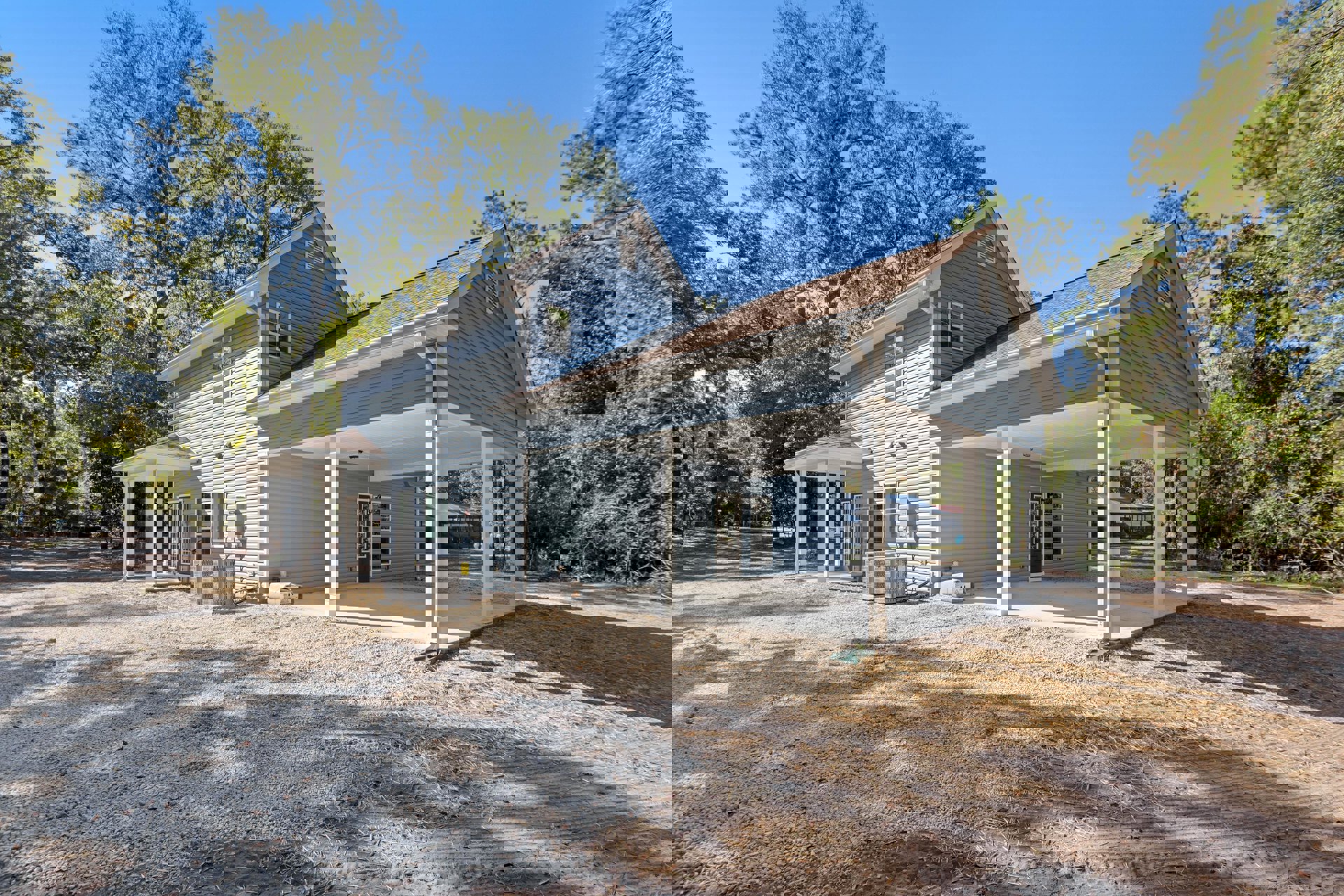 Modern home with covered patio, white siding, large windows, metal utility boxes on lawn, mature trees in background