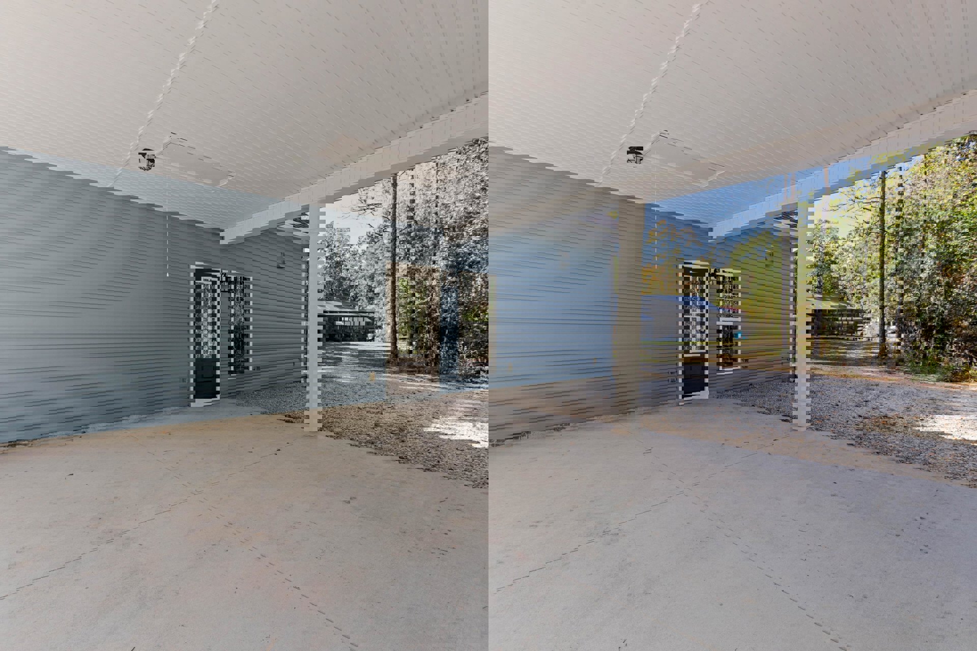 Concrete patio with brown door, white column, and wood-paneled ceiling beneath covered outdoor area; white-framed window and composite exterior finishes visible.