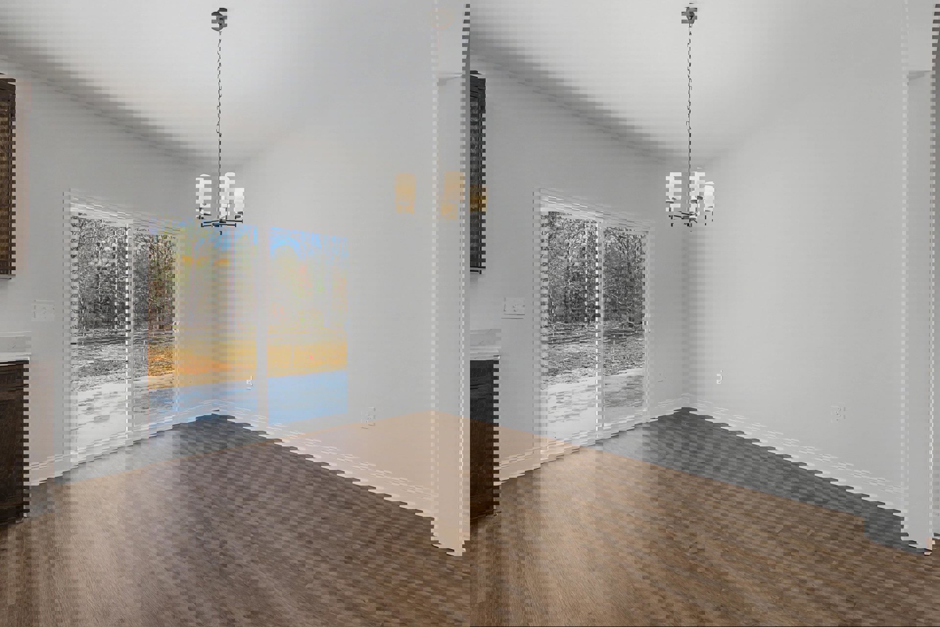 Wood flooring and white plaster walls in a den with a sliding glass door overlooking trees, chandelier hanging from a long chain, close-up of wood surface visible.