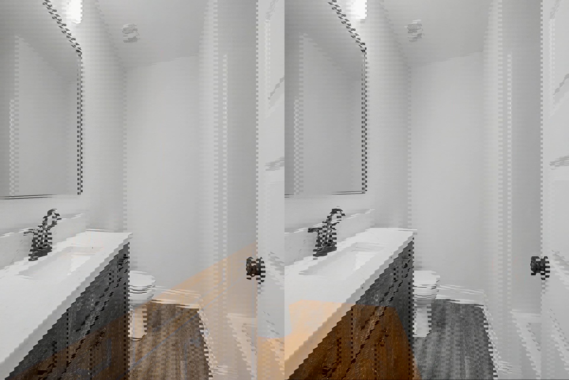 Bathroom with white tile walls, black faucet on a rectangular sink, wood cabinetry, wall-mounted mirror with overhead light, toilet with lid up, ceiling vent visible