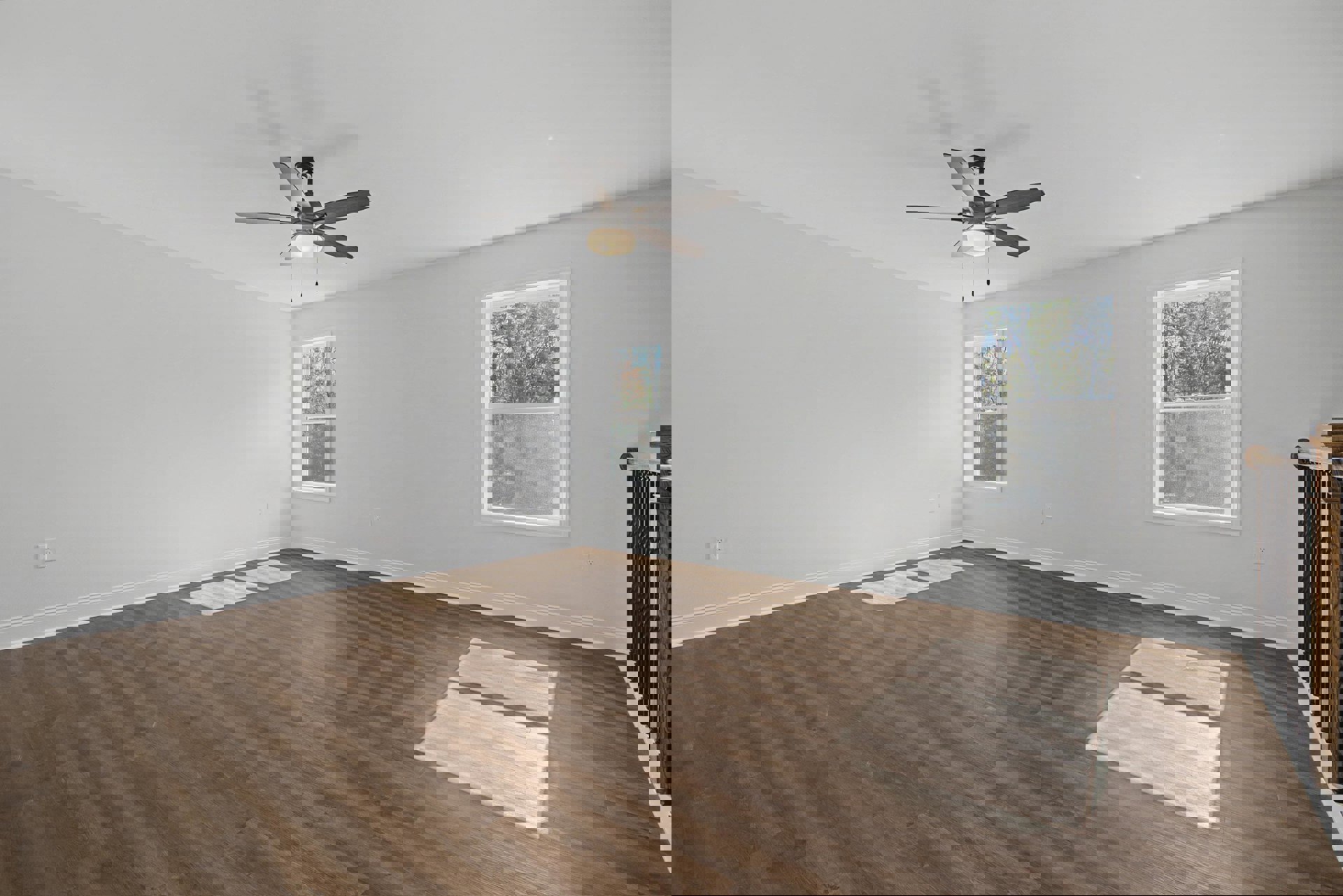 Ceiling fan with light fixture above wood laminate flooring, white plaster walls, large windows framing leafy trees outside