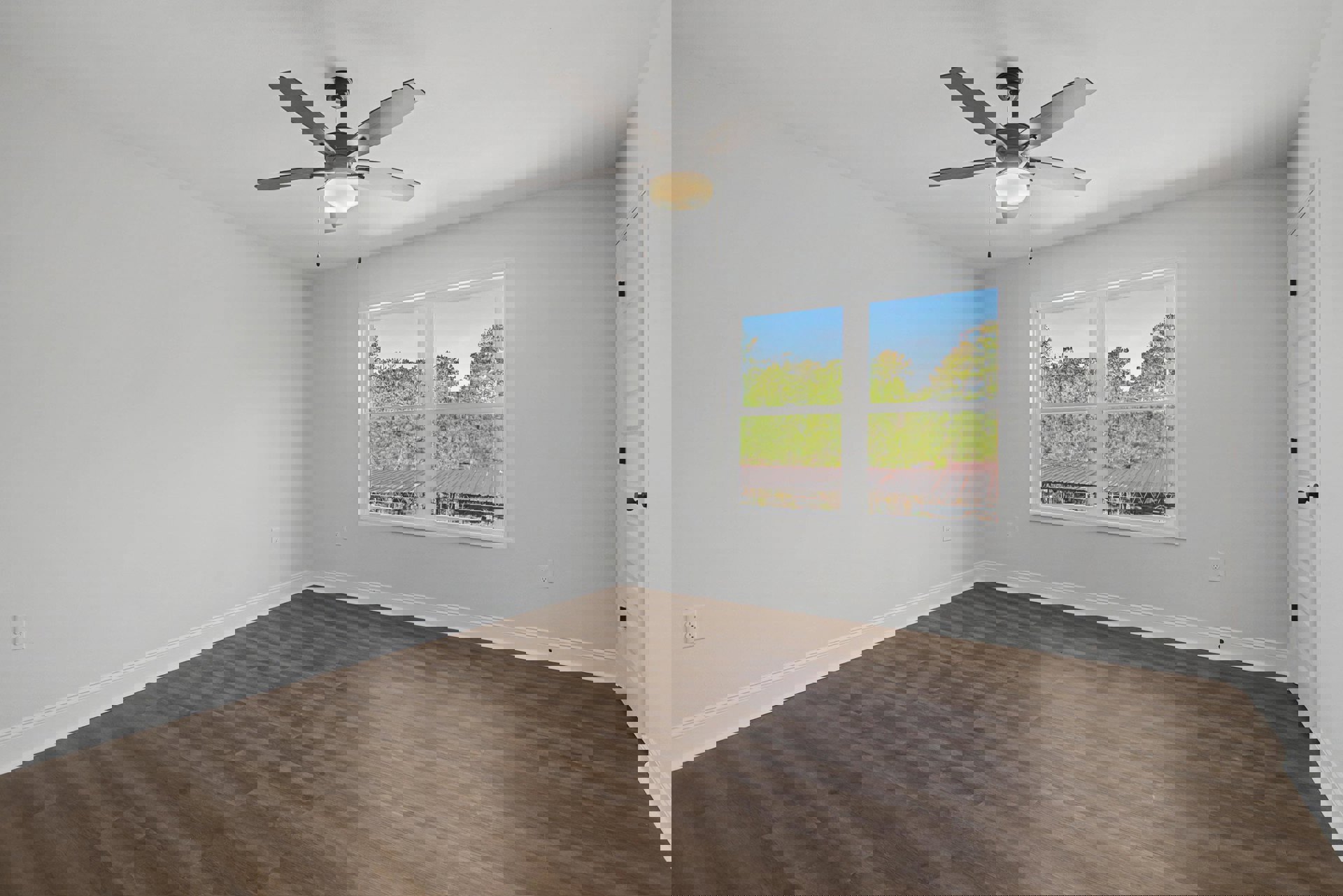 Ceiling fan with round light fixture, white-framed window overlooking trees, wood laminate flooring, pale plaster walls