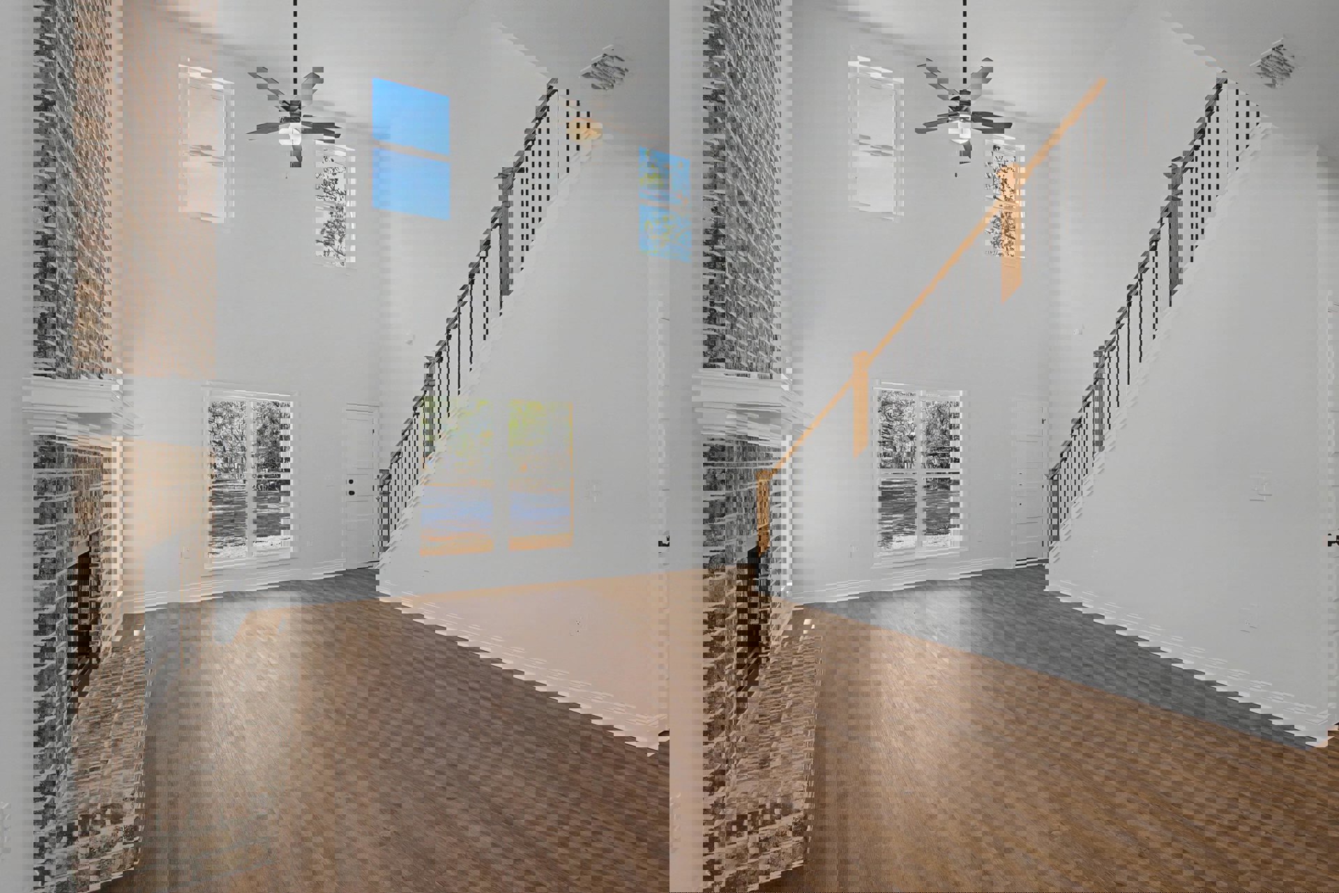 Wood flooring in a bright room with a ceiling fan, large window showing tree branches and greenery outside, white plaster walls