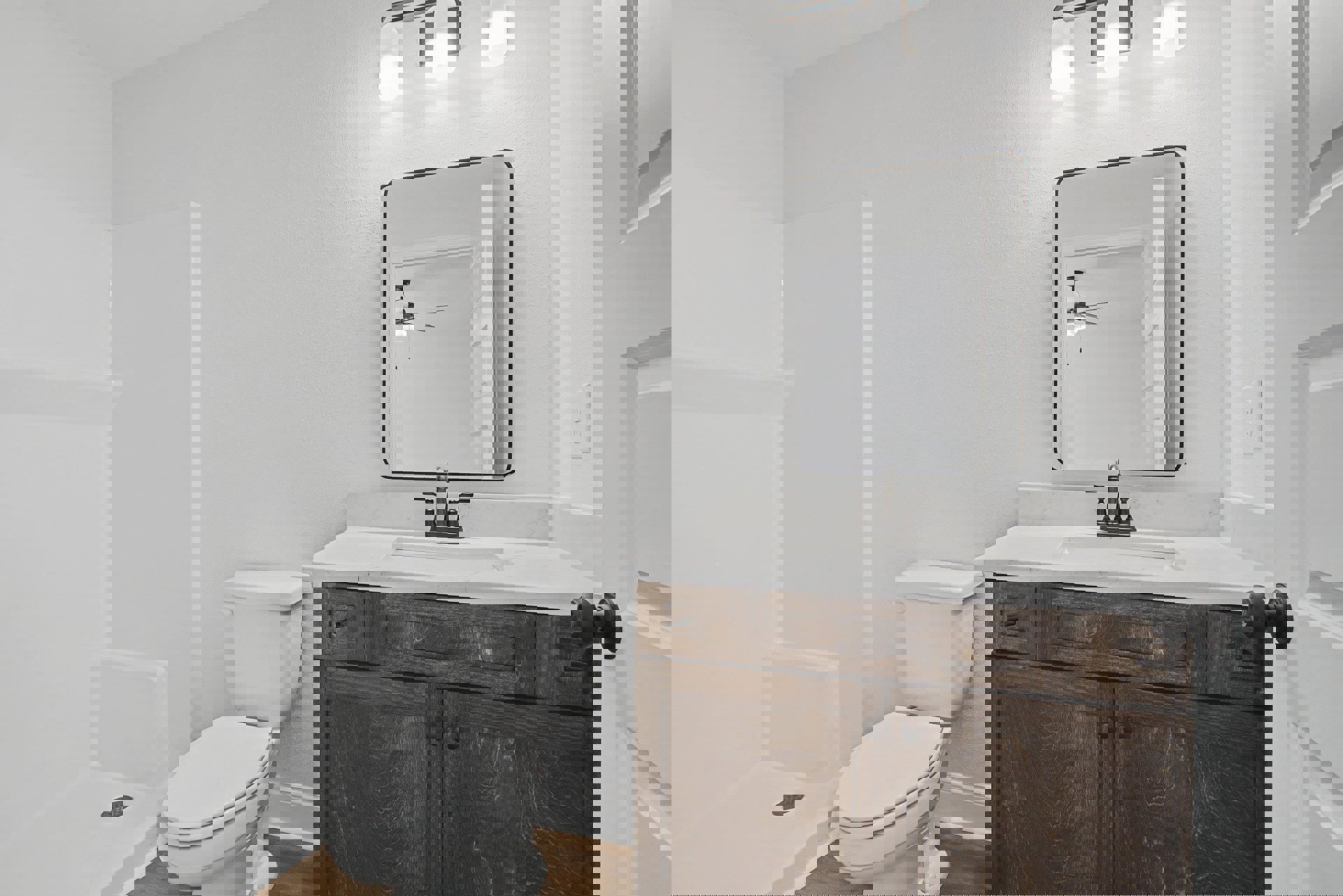 Modern bathroom featuring a rectangular mirror above a white sink with chrome faucet, white toilet with closed lid, light-colored tile walls, and a granite countertop.