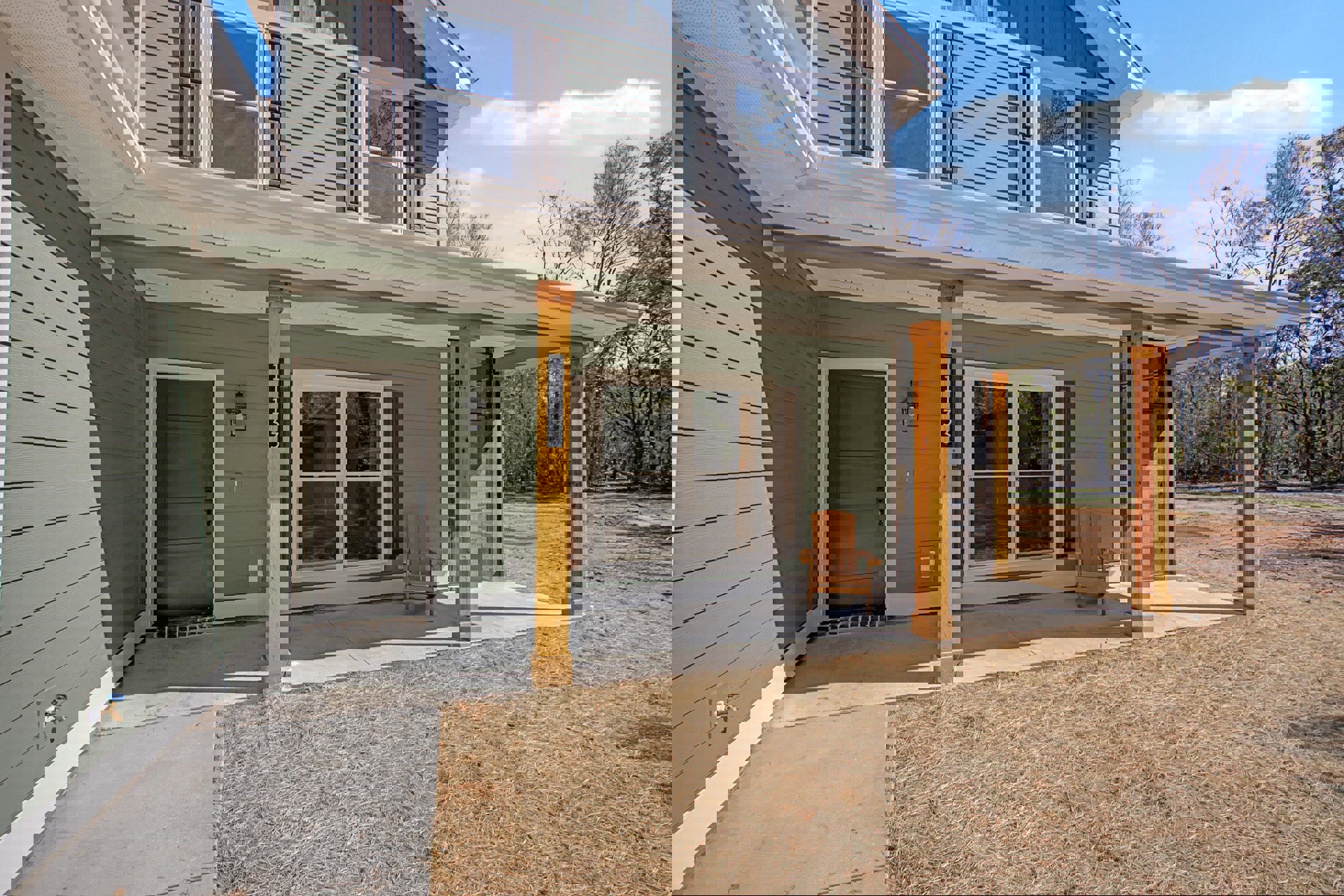 Two-story home with white siding, glass-paned windows, wooden porch featuring a single chair, manicured lawn, and black-framed accents on posts and door.