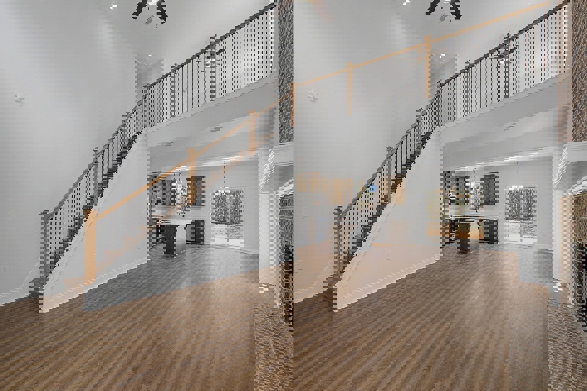 Open kitchen with wood flooring, white countertop island, adjacent staircase featuring metal railings, plaster walls, and ceiling vent with recessed lighting