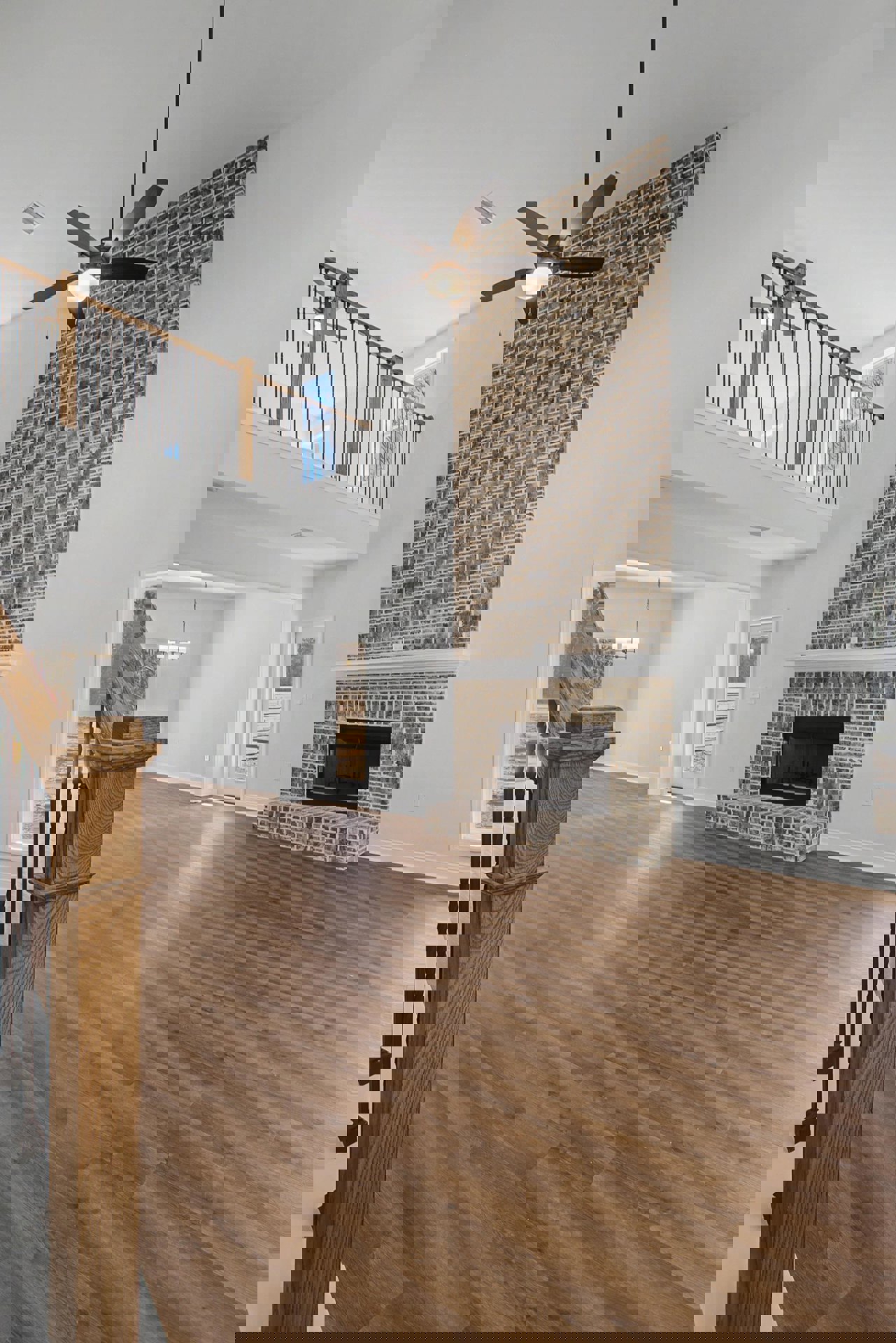 Living room with hardwood floors, brick fireplace, ceiling fan with light, white walls, and a window showing city view