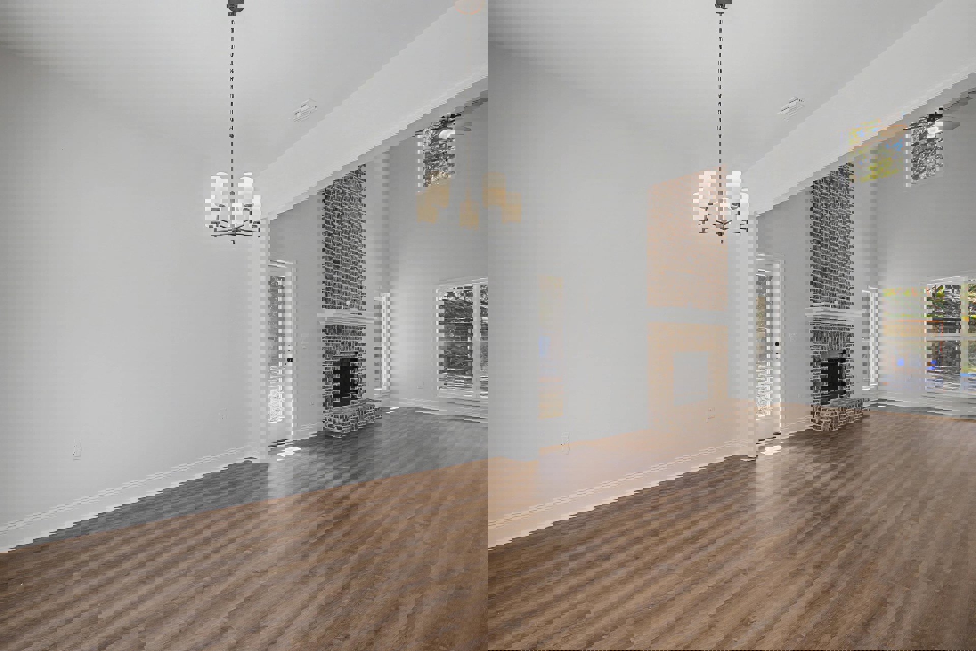Living room with hardwood flooring, white plaster walls, black-framed fireplace, ceiling fan, chandelier, and window overlooking backyard shed