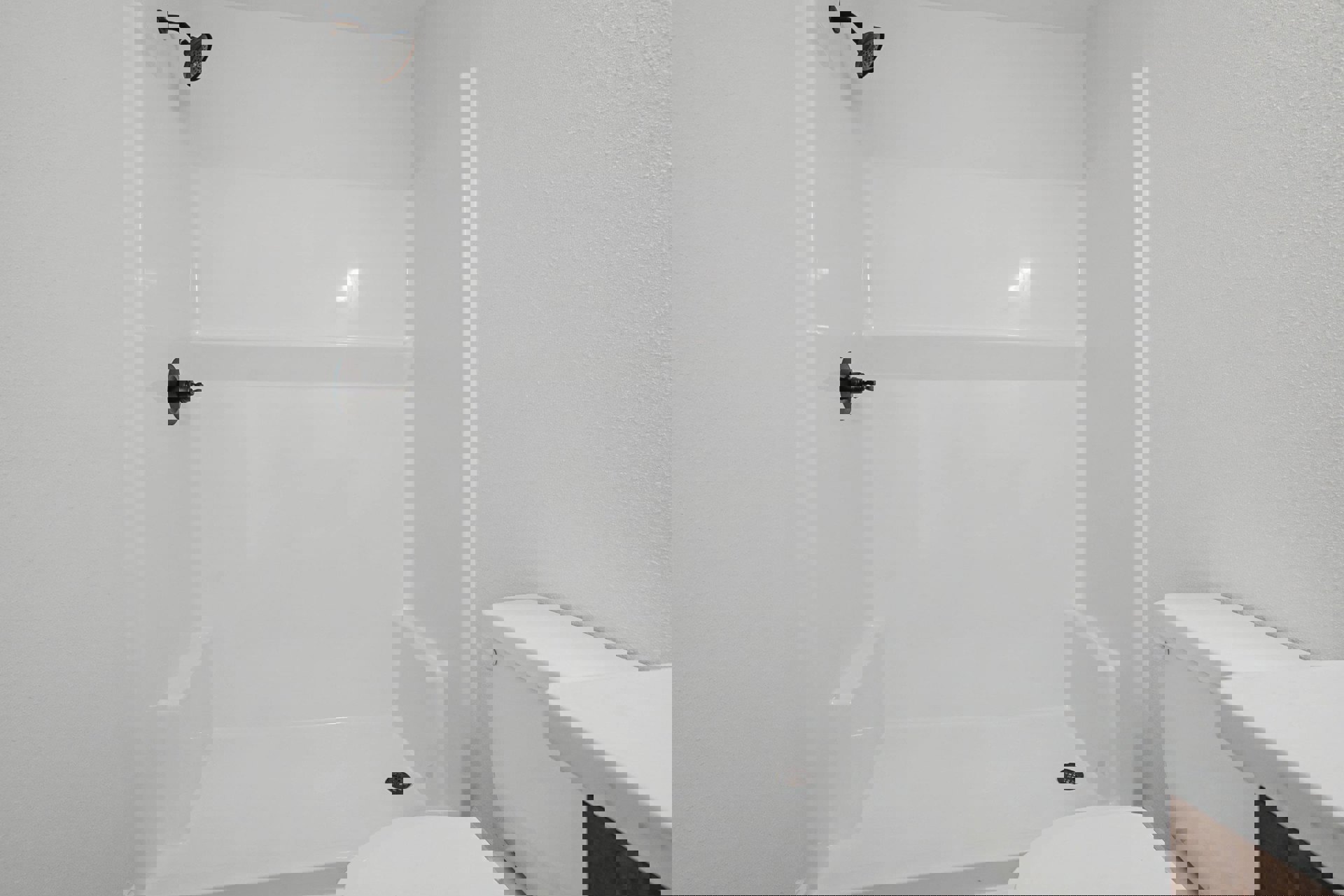White tile shower with chrome showerhead spraying water, adjacent to modern white toilet, bathroom walls and fixtures in neutral tones.