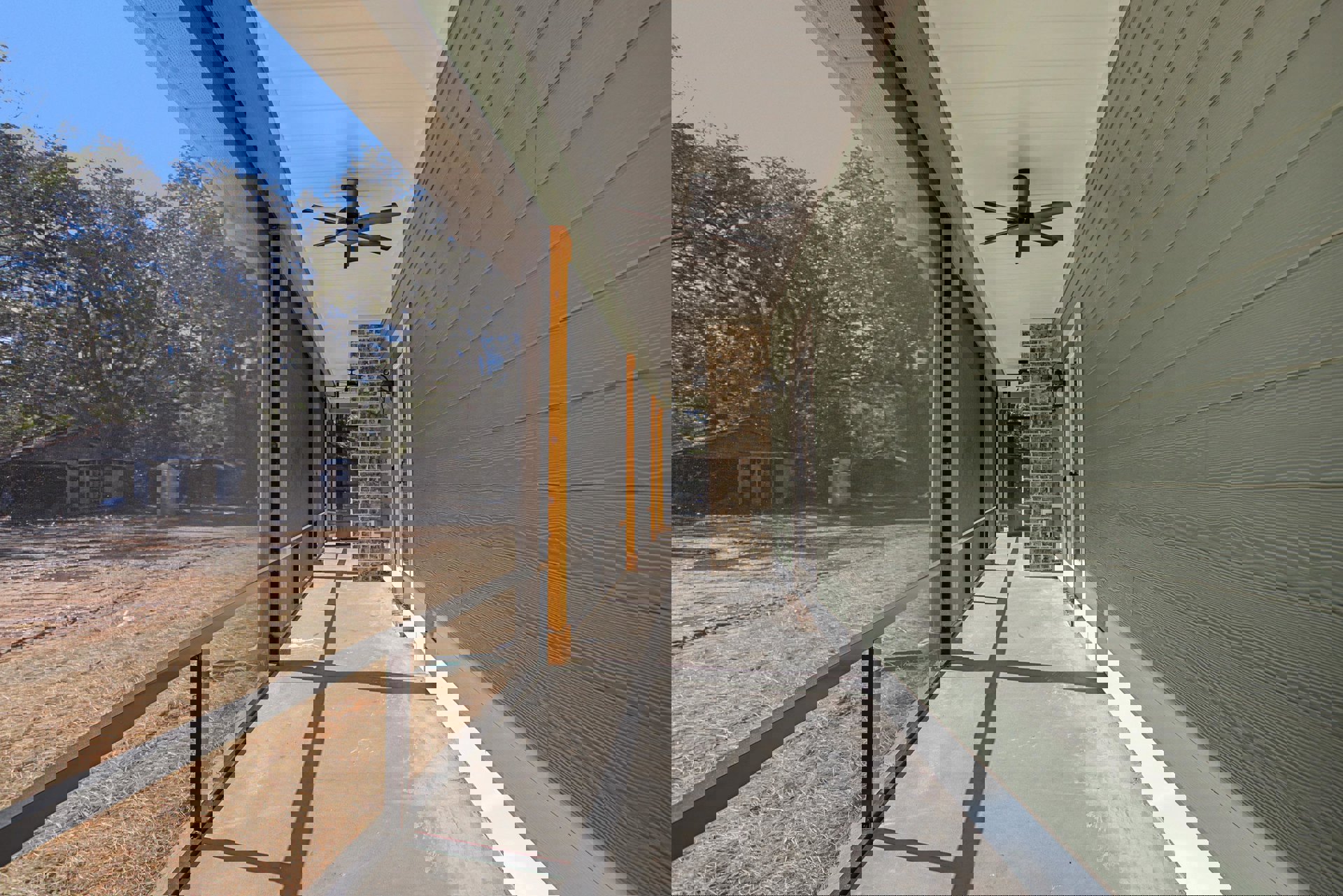 Covered porch with four-blade ceiling fan, screened door, brick wall with lantern, fenced deck overlooking dirt field and trees, portable toilet visible in background