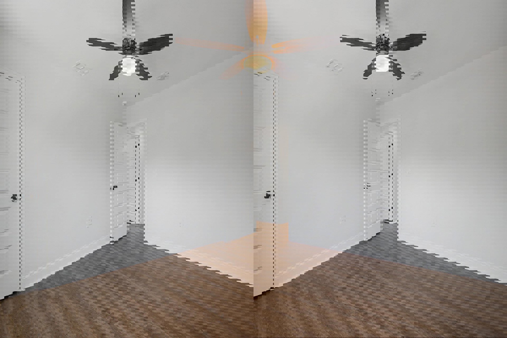 Ceiling fan with light fixture mounted above wood floor, white paneled door, and neutral walls in residential room