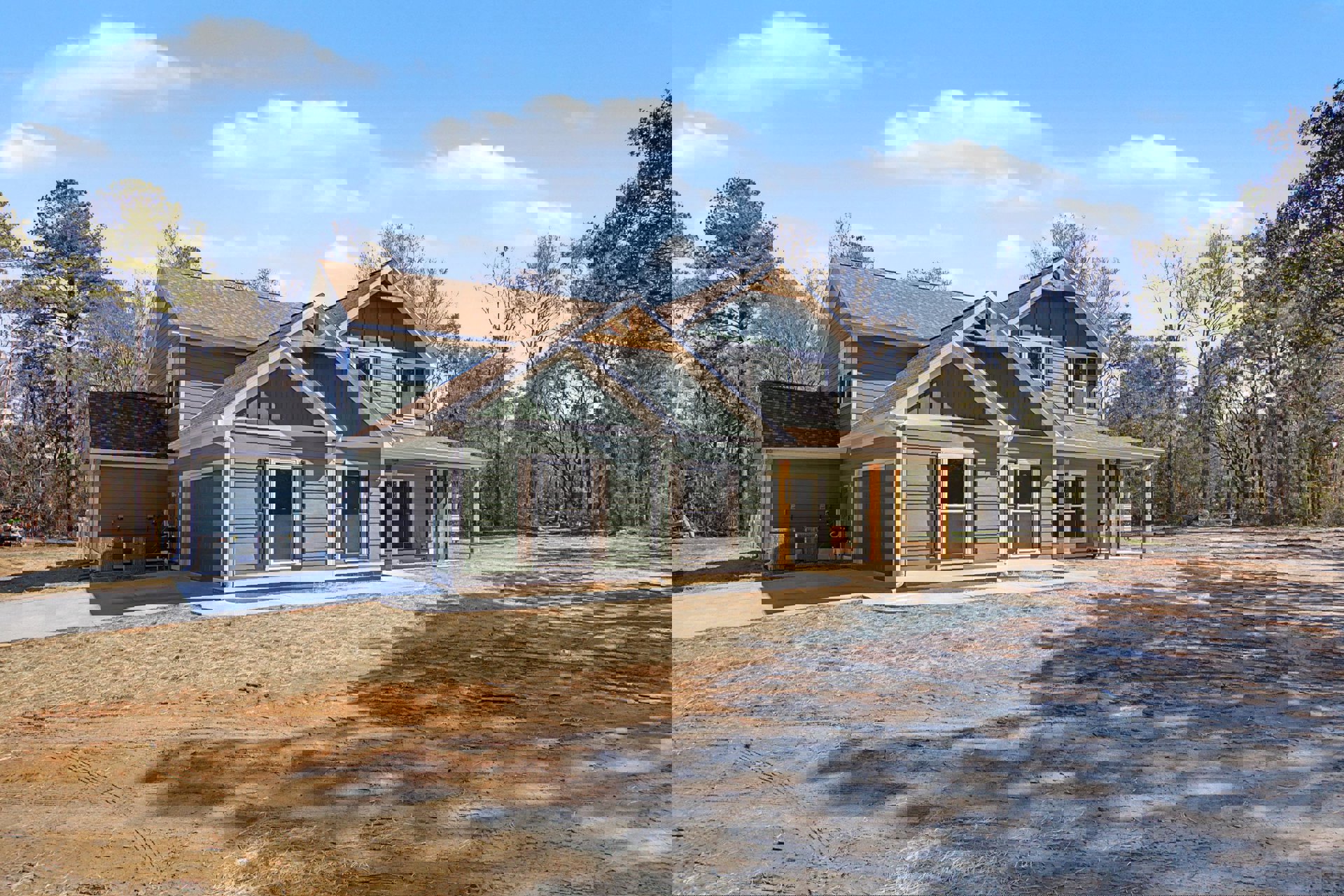 Two-story home with gray siding, white trim windows, shingled roof, paved driveway, and mature trees in the background
