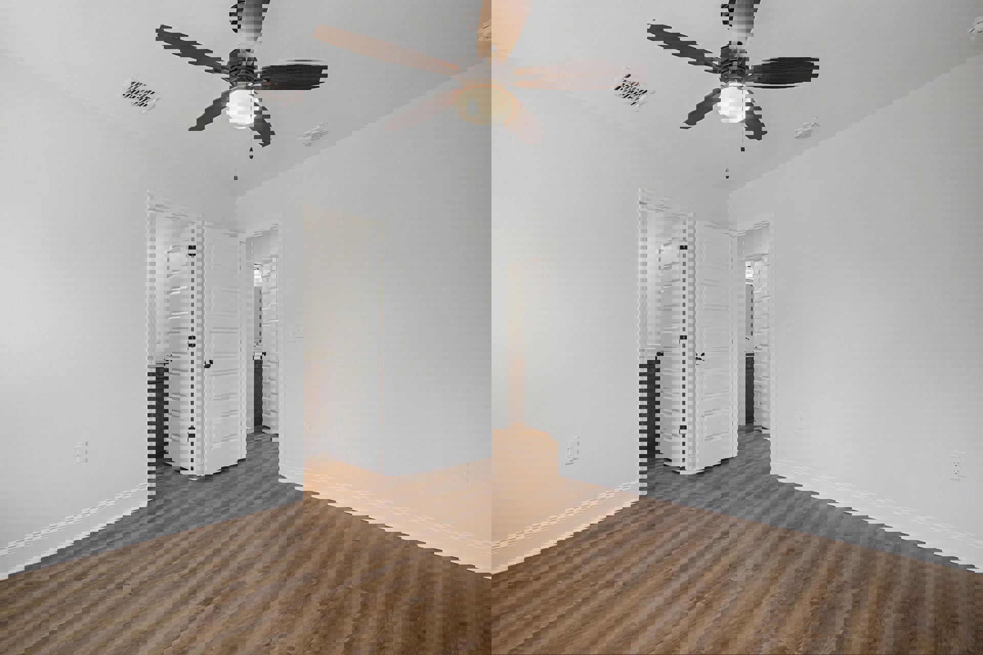 Ceiling fan with light fixture mounted above wood floor, white door with black knob, white baseboards, and ceiling vent in a modern room