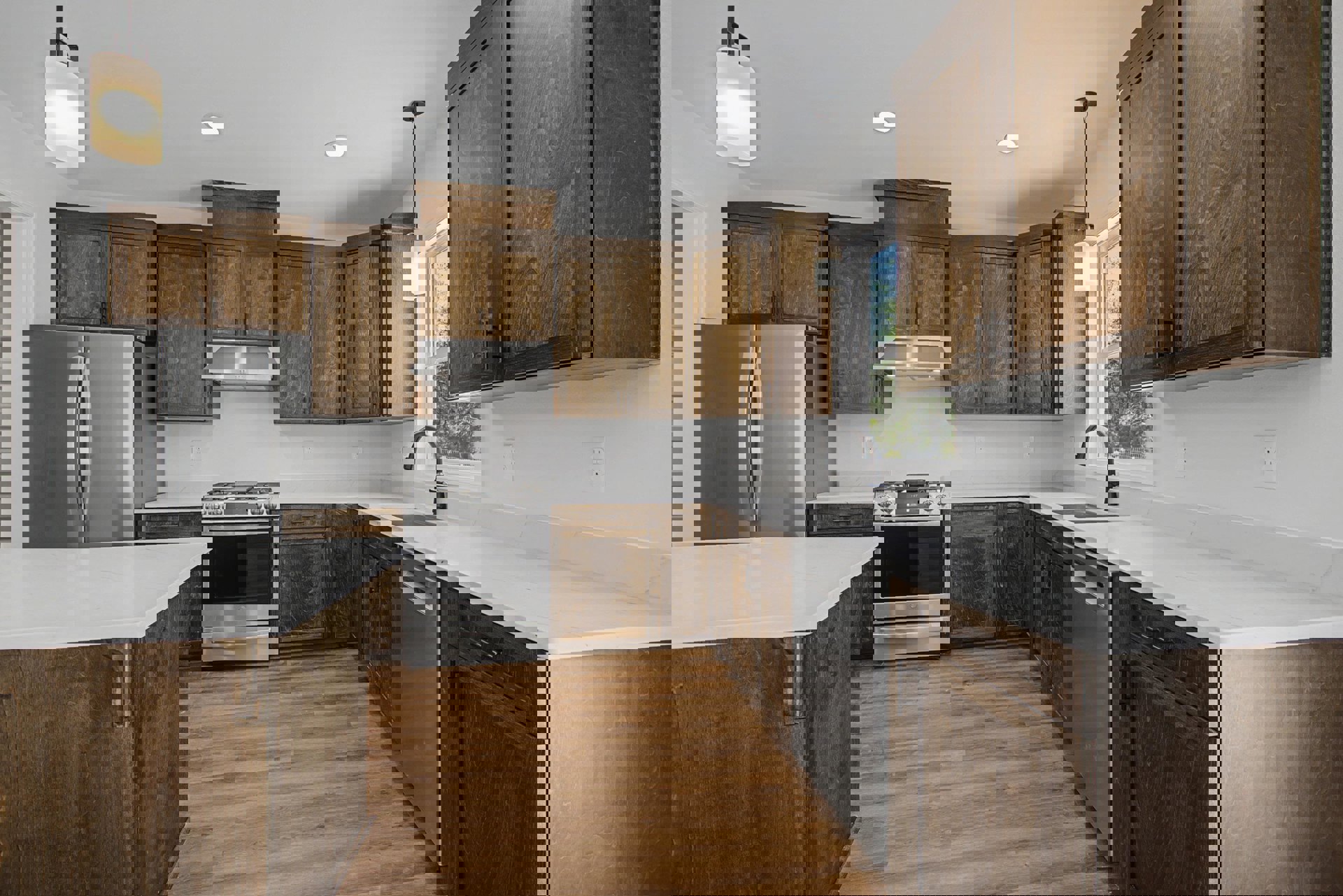 Kitchen with natural wood cabinets, granite countertops, stainless steel stove and refrigerator, white pendant light fixture, and wood flooring.