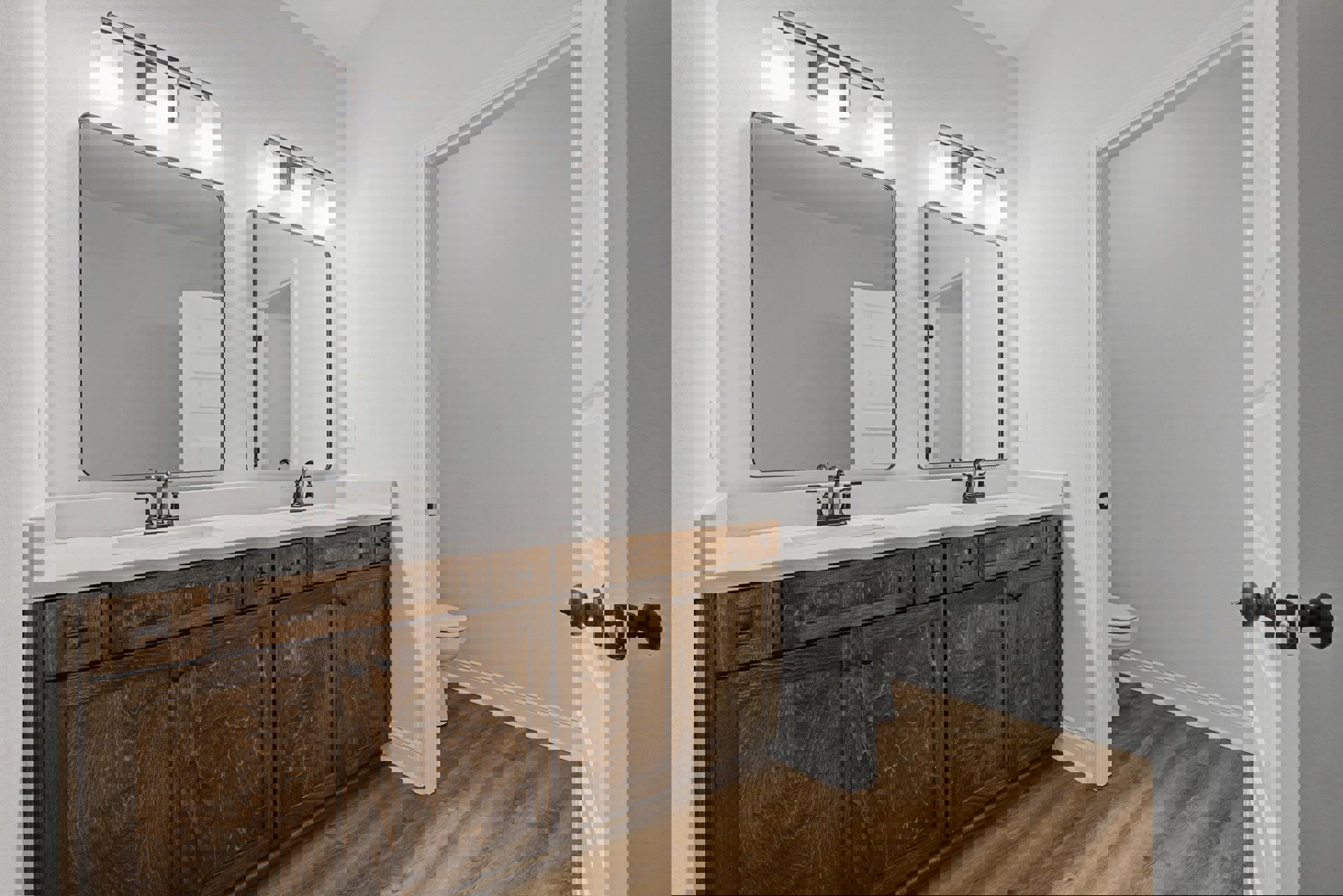 Bathroom with double sinks, white countertops, matching mirrors above each sink, toilet visible near glass wall, tile flooring, white cabinetry, chrome faucets, open door revealing