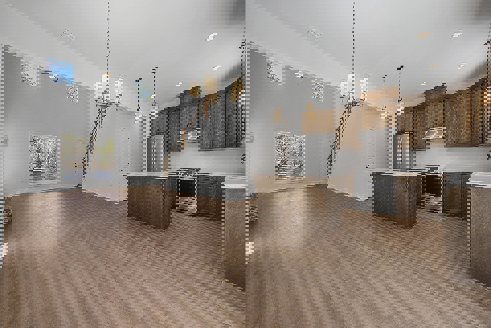 Open kitchen and living room featuring wood floors, white walls, wooden counter with white top, stainless steel stove and refrigerator, cabinetry, large window overlooking trees