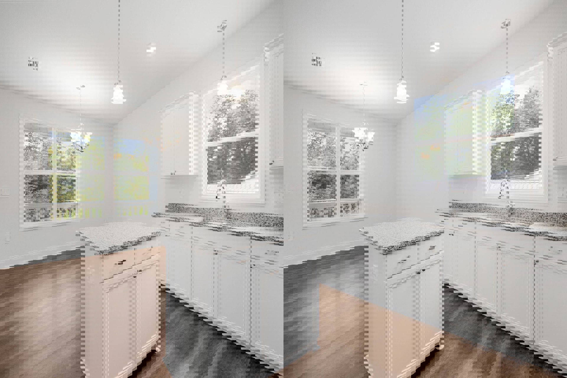 White kitchen with marble countertops, white cabinetry, stainless steel appliances, large window above sink overlooking trees, white kitchen island with granite top, pendant light