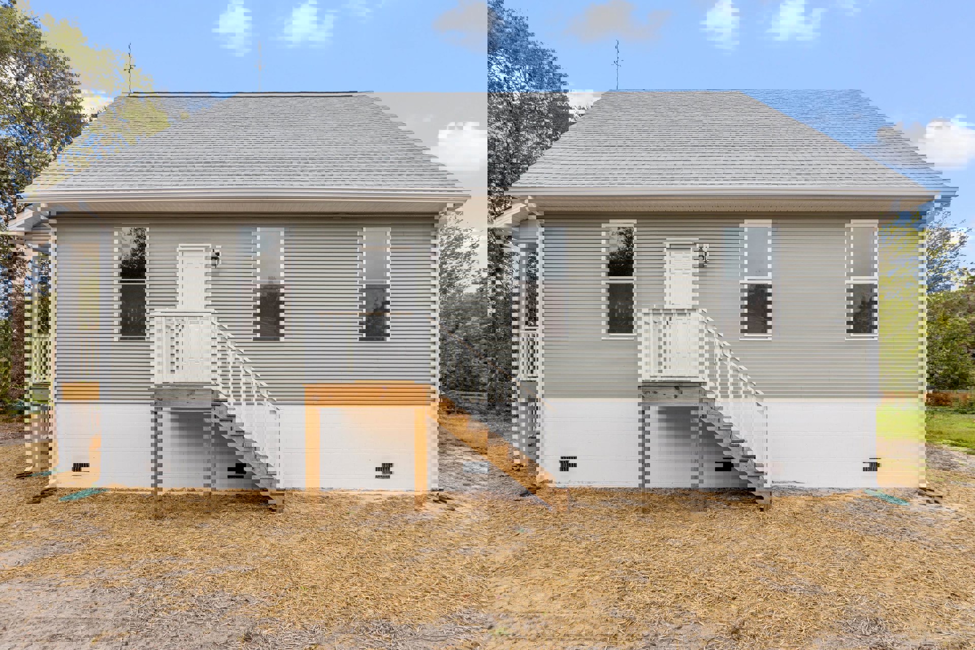 Two-story home with white-framed windows, wooden exterior staircase leading to porch, straw-covered ground, trees reflected in glass.