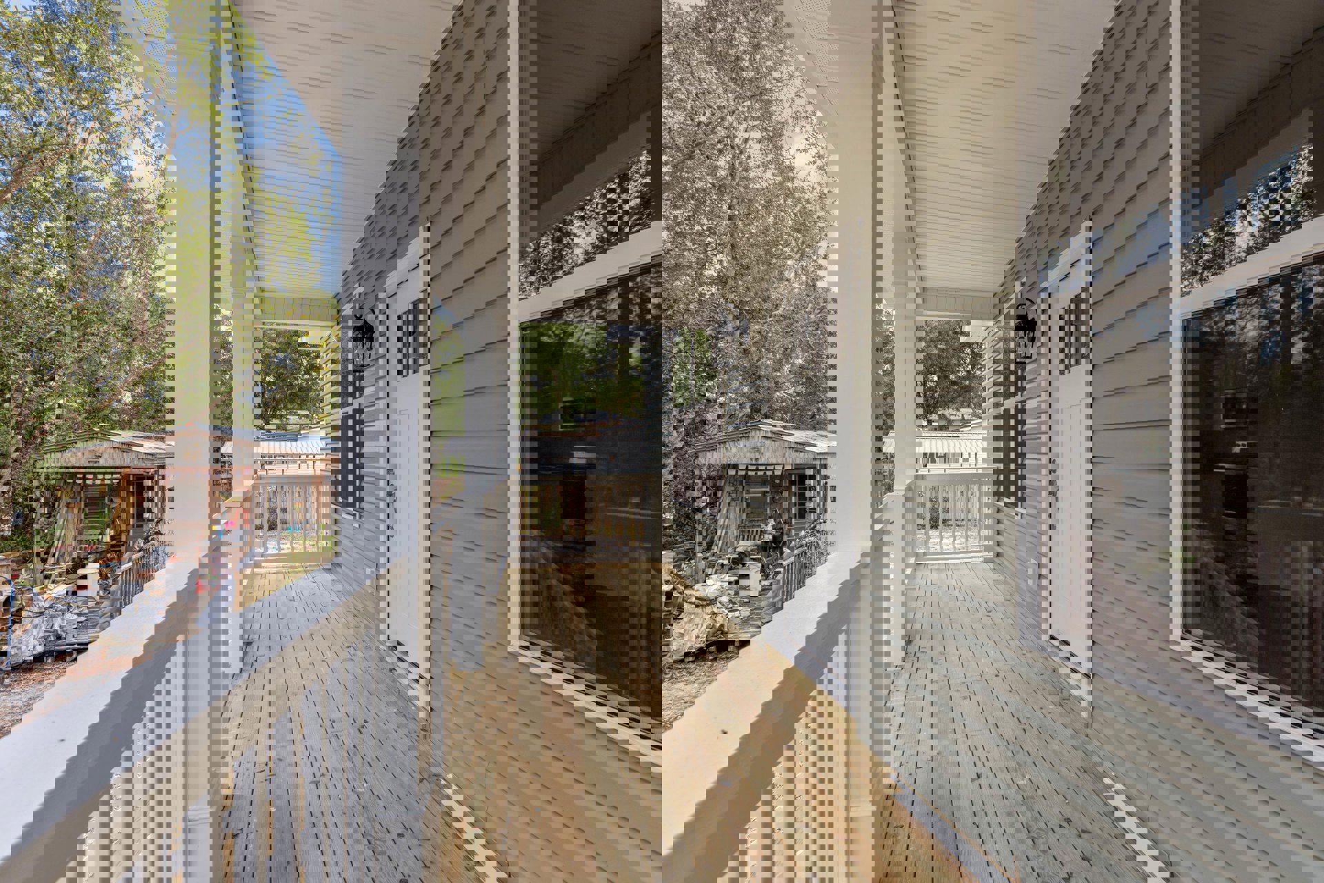 Covered porch with white railing, wood decking, and glass door, surrounded by trees and a fenced yard