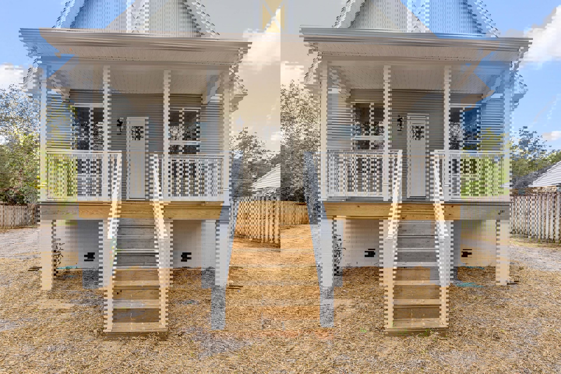 Wooden stairs and porch with white door, wooden fence, and tree with green leaves in front of a residential home