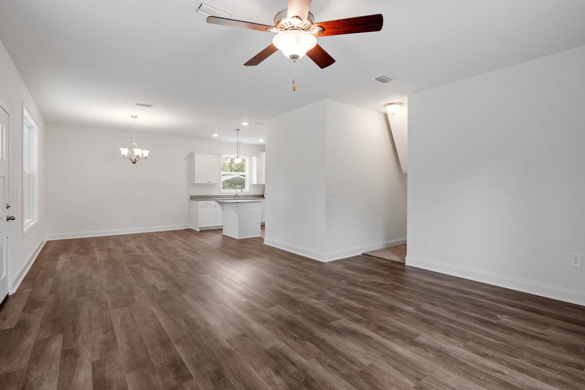 Ceiling fan with light fixture above wood flooring, white walls, white columns, and window.