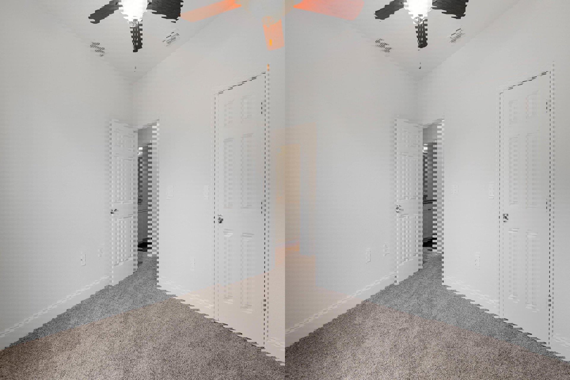 Carpeted room with two white doors, silver door knobs, and a ceiling fan with light fixture on a plaster ceiling