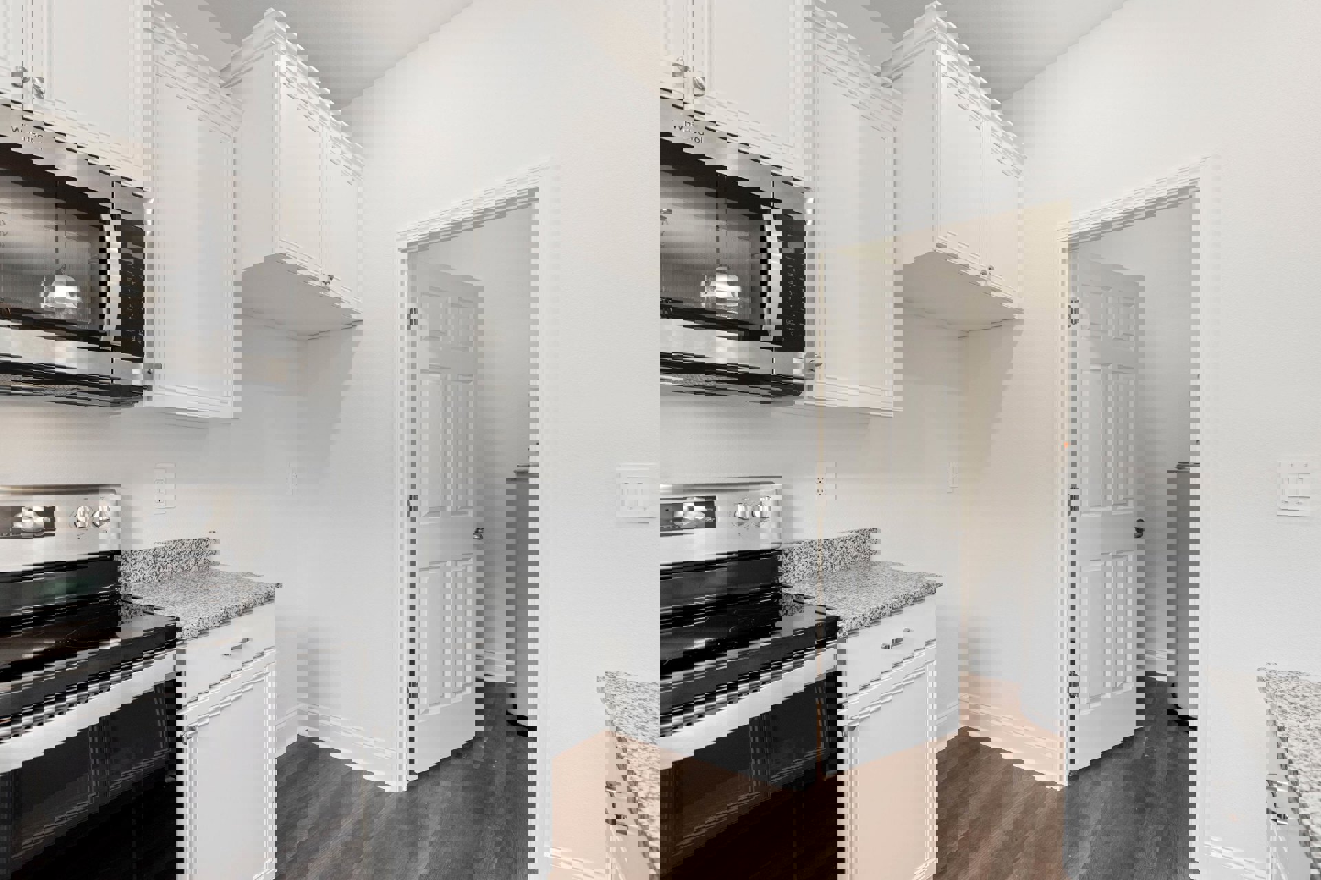 White kitchen cabinets with silver knobs, stainless steel stove and microwave, light-colored countertop, overhead ceiling light, white door with silver doorknob.