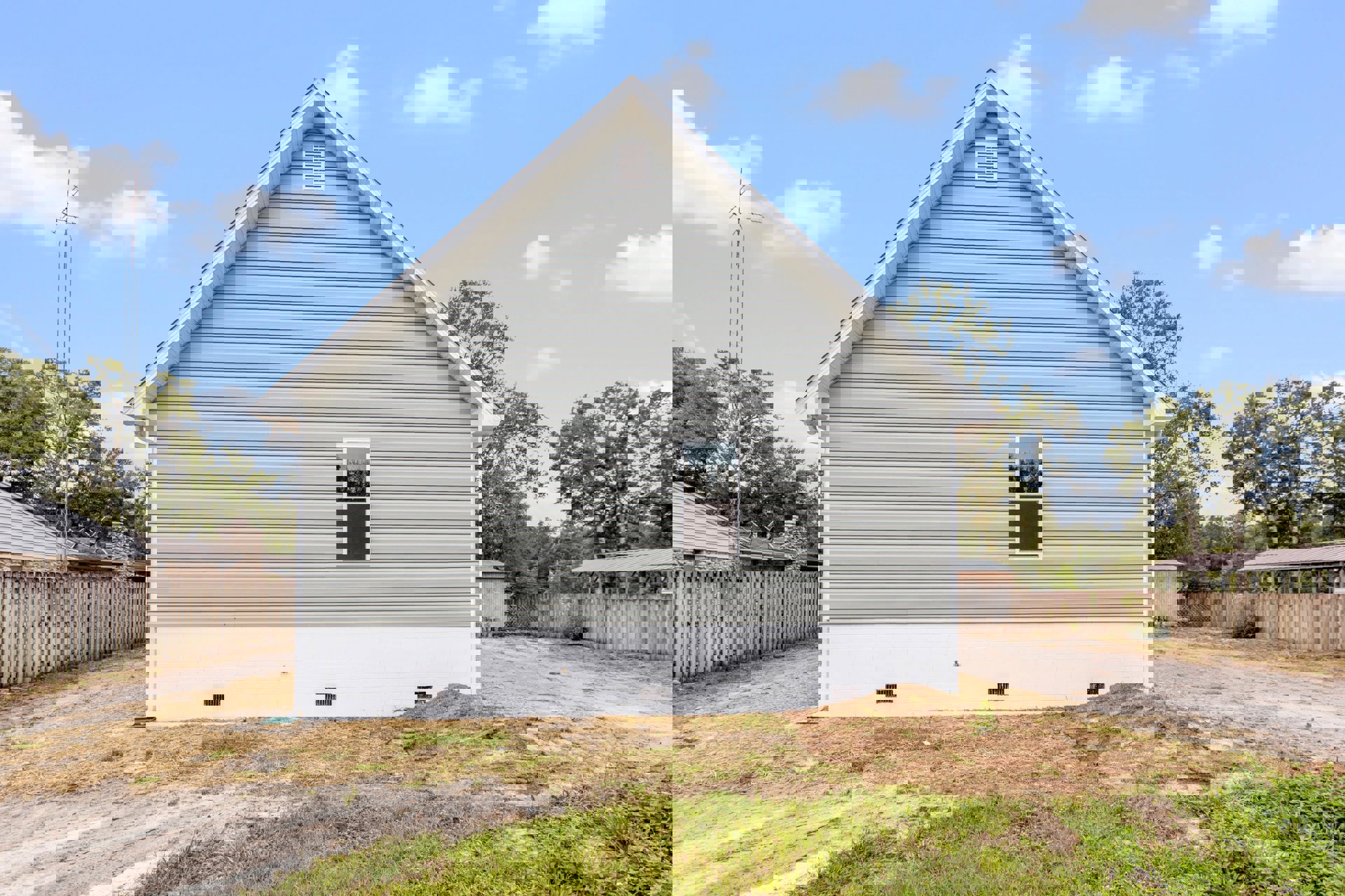 White-roofed house with white walls, white-framed windows, wooden fence, stone accent, grassy yard, and exterior vent under a partly cloudy sky.