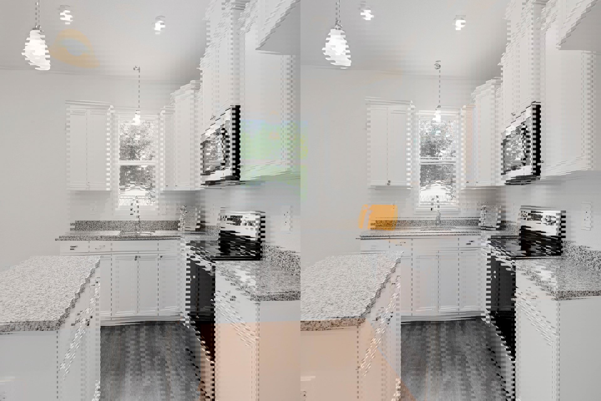 White kitchen cabinets and granite countertops, open microwave door, window overlooking trees and neighboring house, ceiling light fixture, wooden cutting board with a bow on the