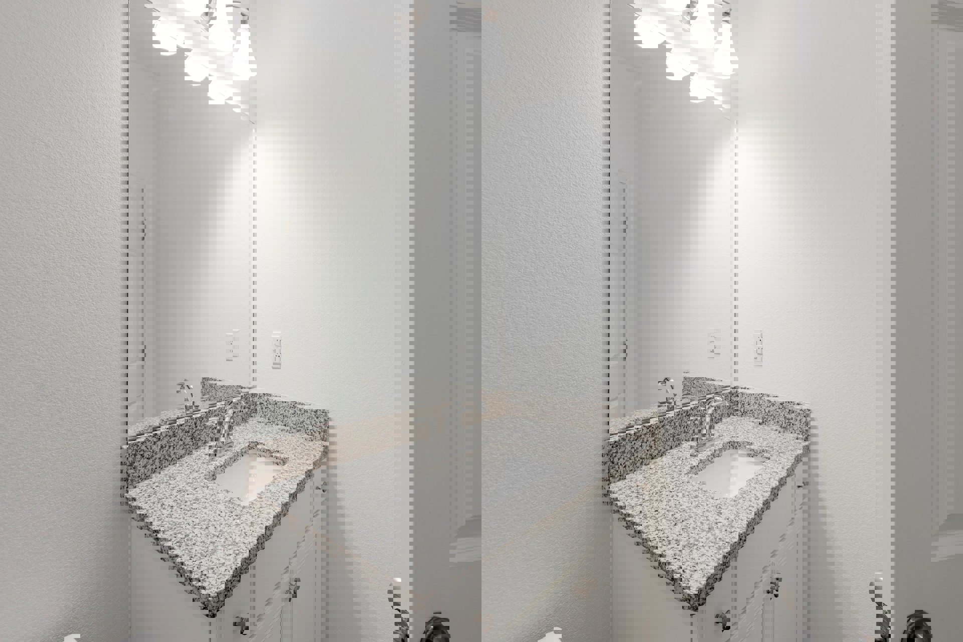 Marble countertop with undermount sink, chrome faucet, large framed mirror, white tile backsplash, and wall-mounted light fixture in a modern bathroom