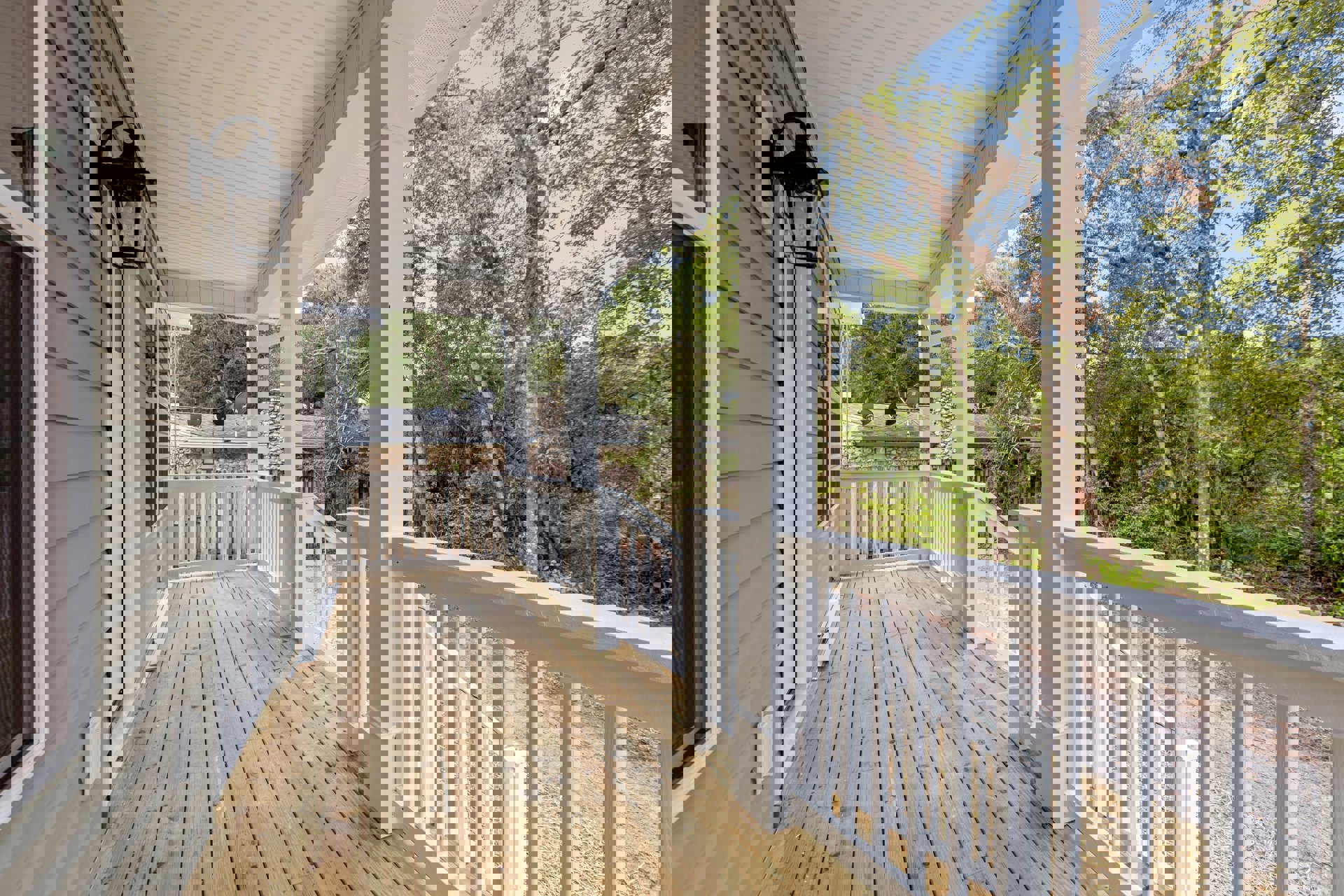 Wood deck porch with white railing and pillars, outdoor lamp, and trees in background