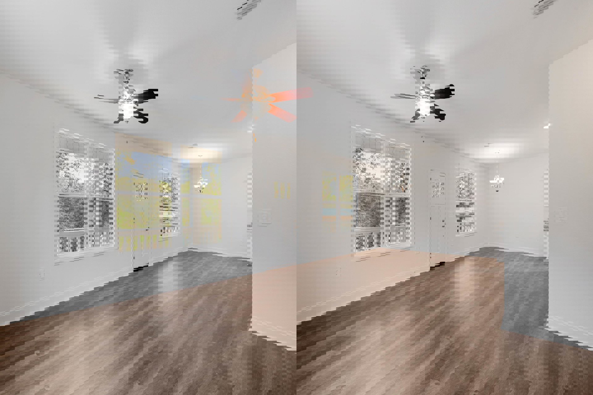 Ceiling fan with light fixture mounted on white plaster ceiling above wood laminate flooring, white door with glass window, large window overlooking porch and trees