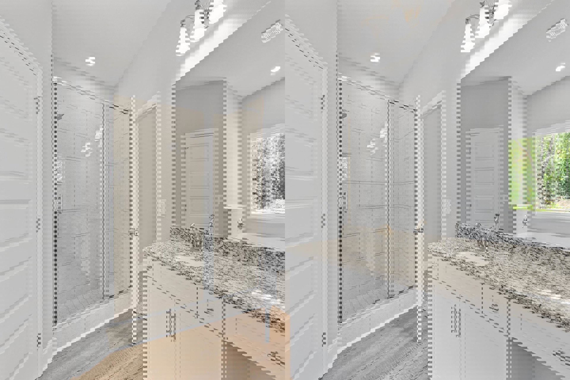 Bathroom featuring glass shower enclosure, marble countertop with undermount sink, white paneled door, and window overlooking leafy trees.