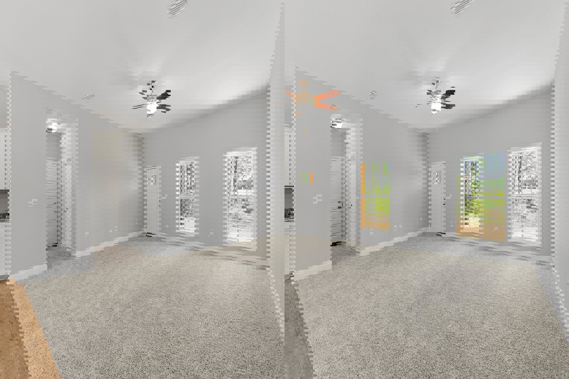 Carpeted room featuring a ceiling fan with light fixture, multiple windows offering views of trees, and a white door with glass inset.