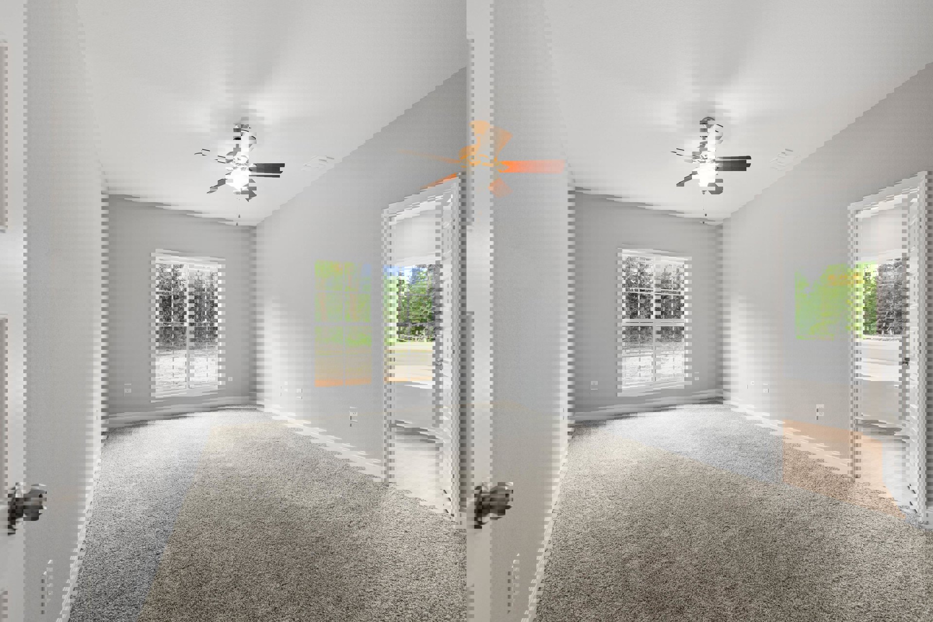 Carpeted bedroom with ceiling fan, white walls, window overlooking trees, open door with silver knob