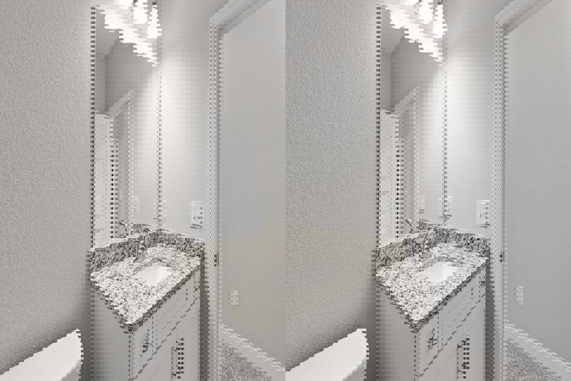 Marble countertop with undermount sink and chrome faucet, large framed mirror above, white walls and door frame, light switch visible on side wall