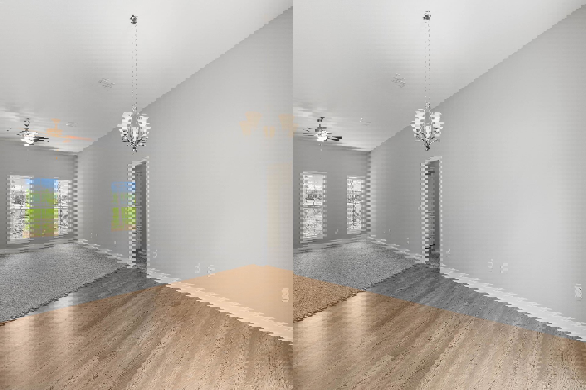 Living room with wide plank wood flooring, ornate chandelier hanging from a plaster ceiling, large windows overlooking a grassy yard and trees, open doorway leading to adjacent